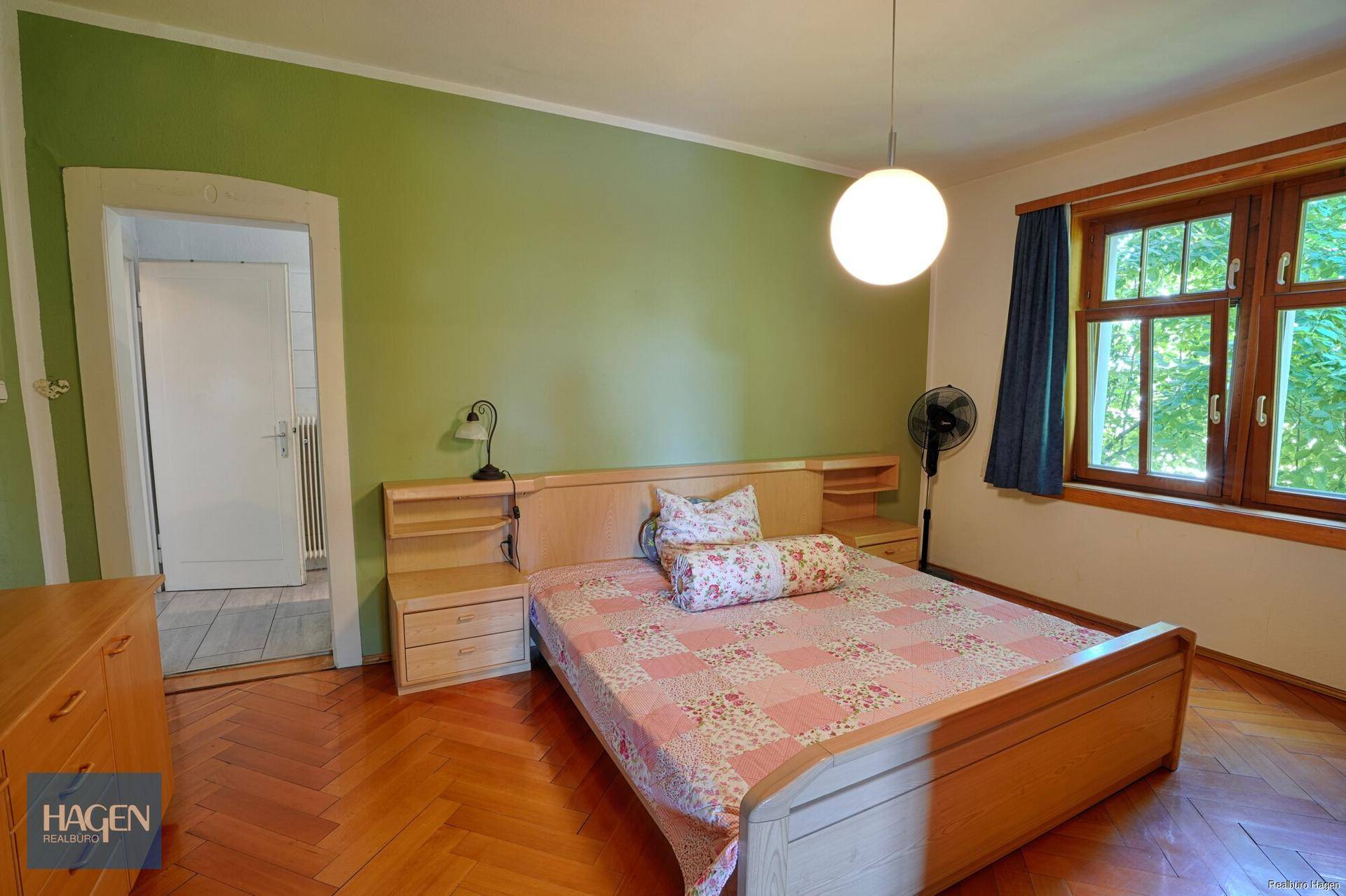 Schlafzimmer mit grün gestrichenen Wänden, Holzparkett und einem großen Fenster.