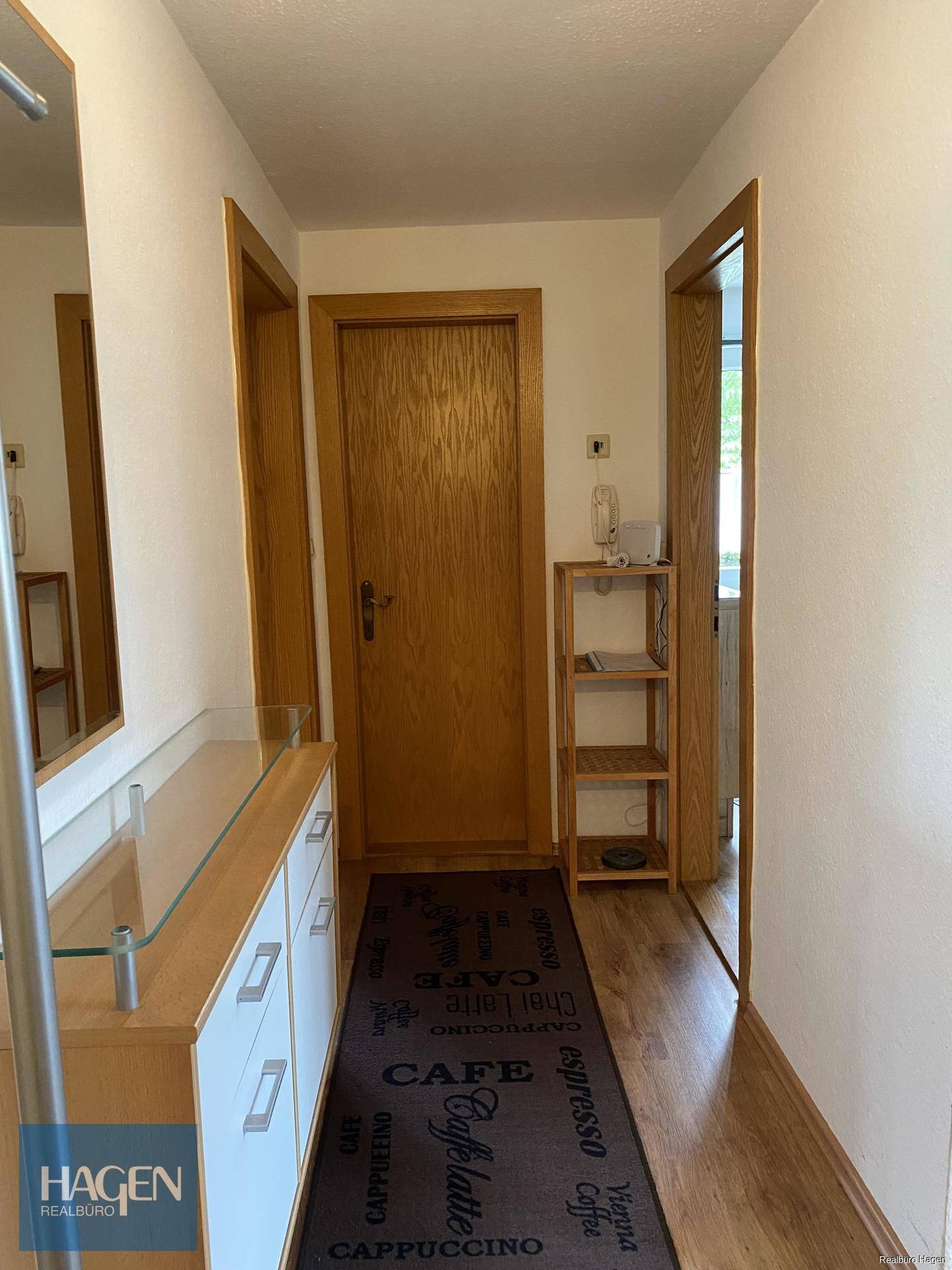 Heller Eingangsbereich mit Holzmöbeln, einem Spiegel und einem Teppichläufer.