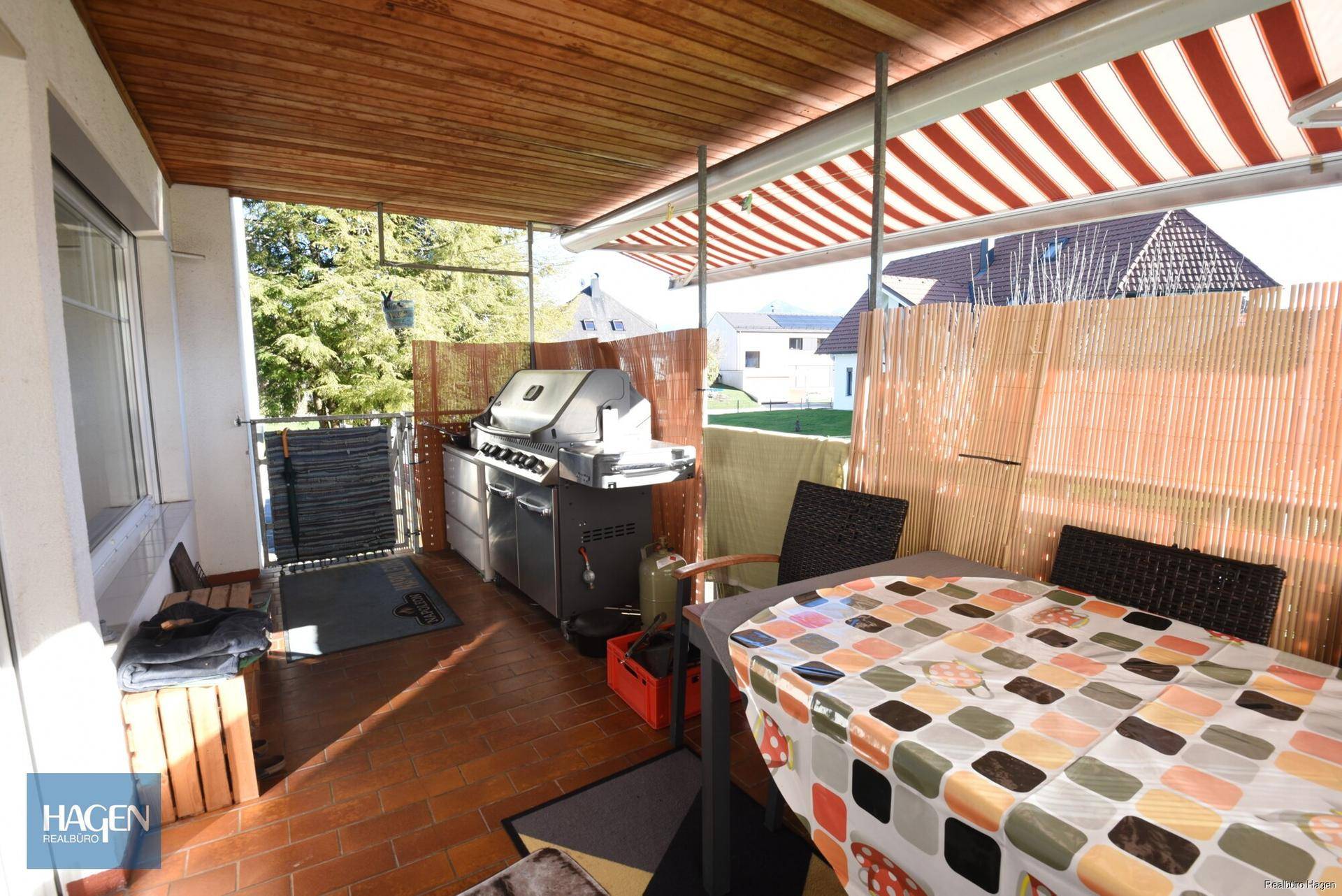 Überdachte Terrasse mit Grillbereich, Esstisch und Markise für sonnige Tage.