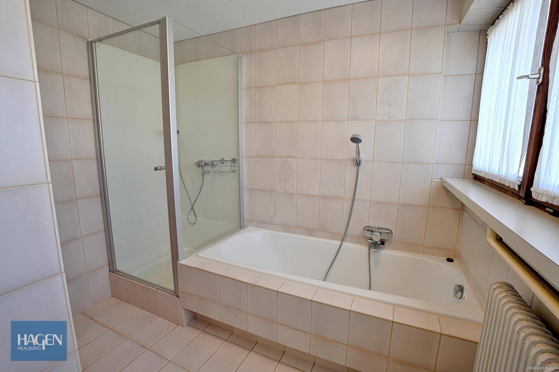 Badezimmer mit Badewanne, Duschkabine und Fenster, gefliest in hellen Tönen.