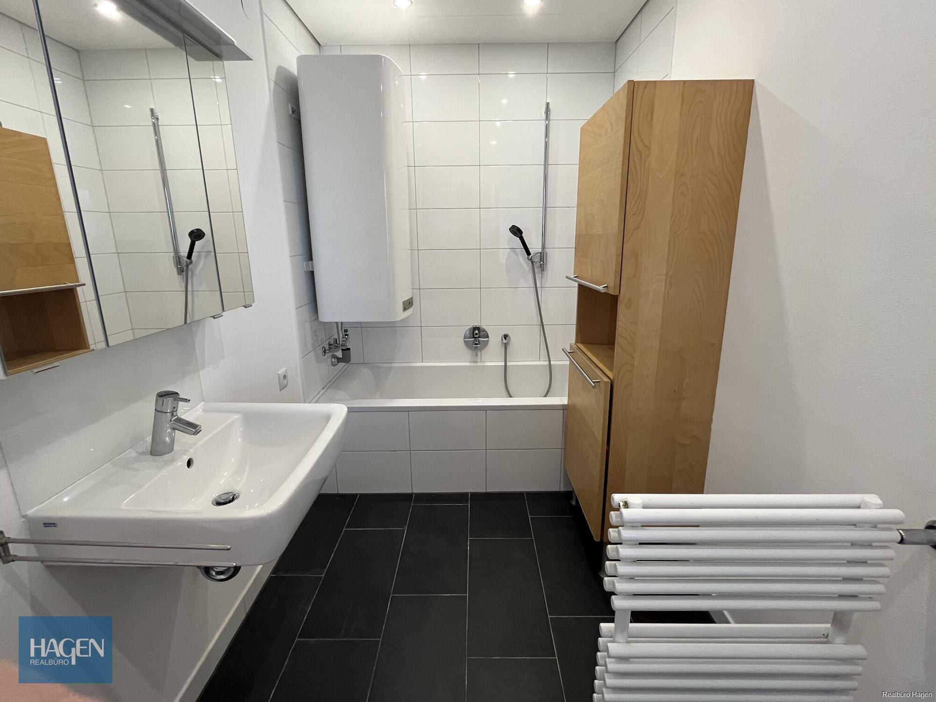 Modernes Badezimmer mit Badewanne, Waschbecken, Spiegel und beheiztem Handtuchhalter.