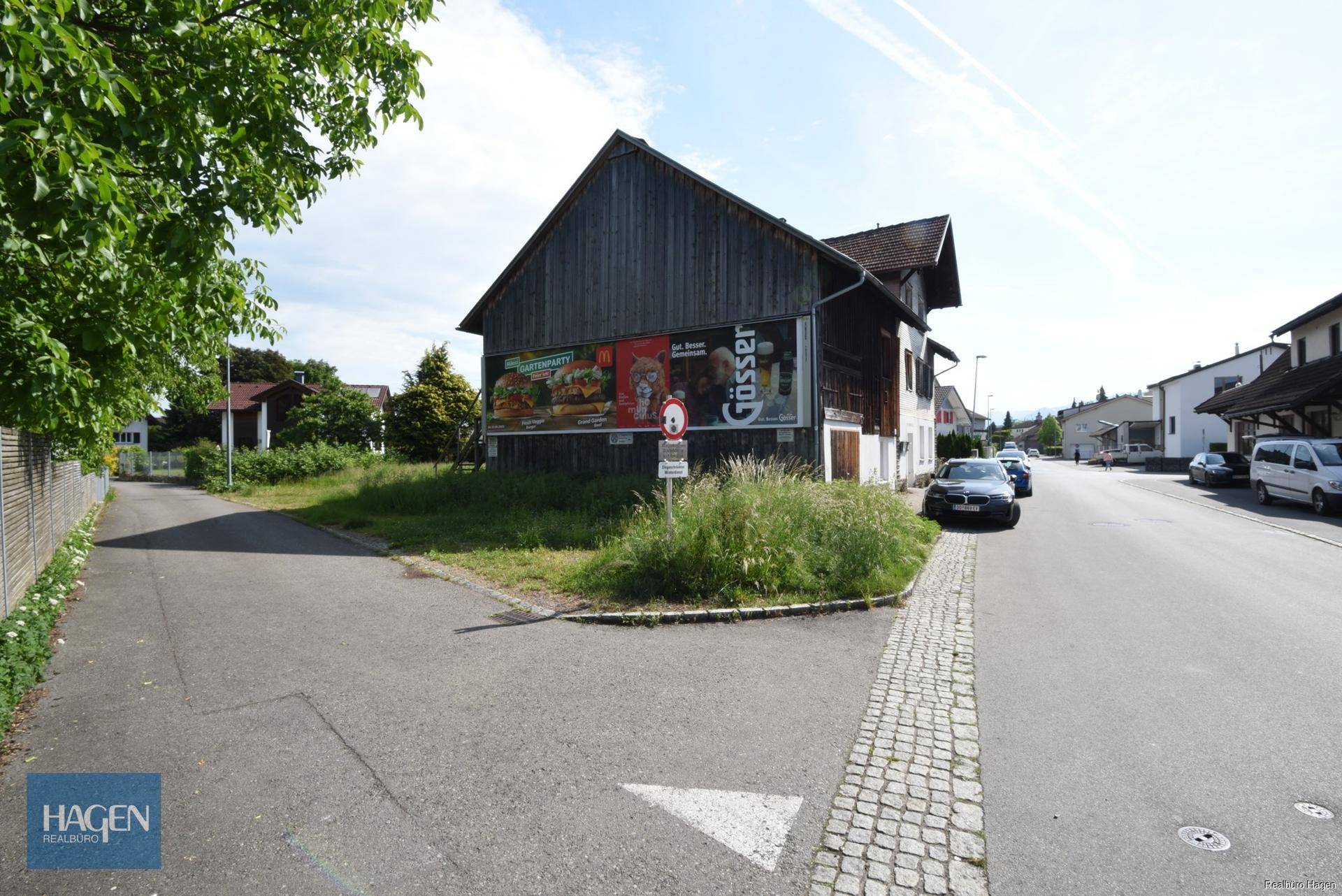 Rückseite eines Gebäudes mit Holzverkleidung, Werbetafeln und angrenzender Straße.