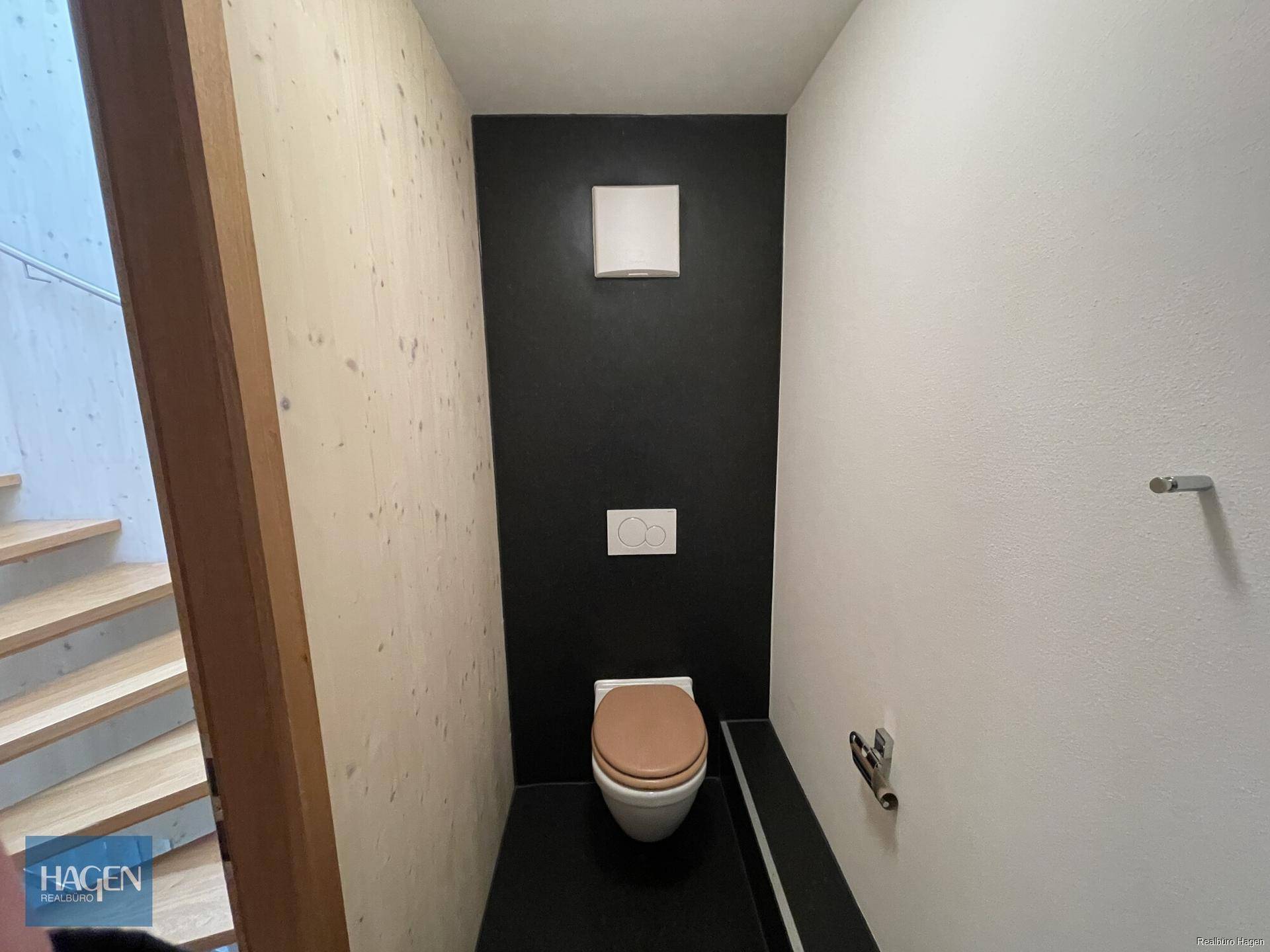 Modernes Gäste-WC mit dunklem Boden, Wand-WC und Holzwand.