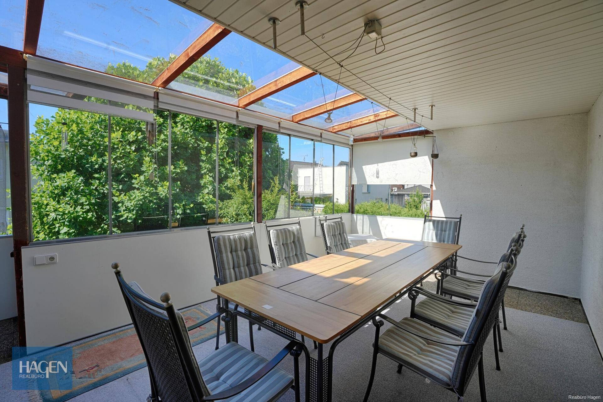 Verglaste Terrasse mit Esstisch und Stühlen, ideal für Mahlzeiten im Freien.