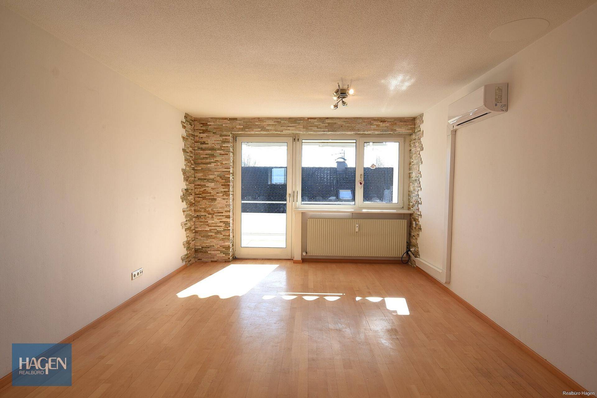 Heller Wohnraum mit Parkettboden, dekorativer Steinwand und Zugang zum Außenbereich.