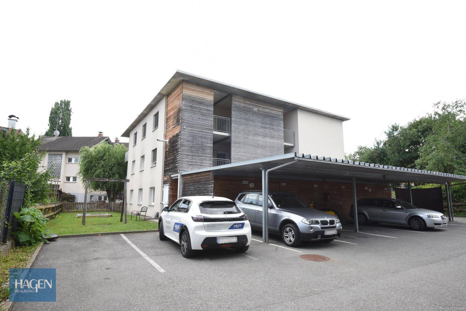 Mehrfamilienhaus mit moderner Holzfassade und überdachten Parkplätzen.