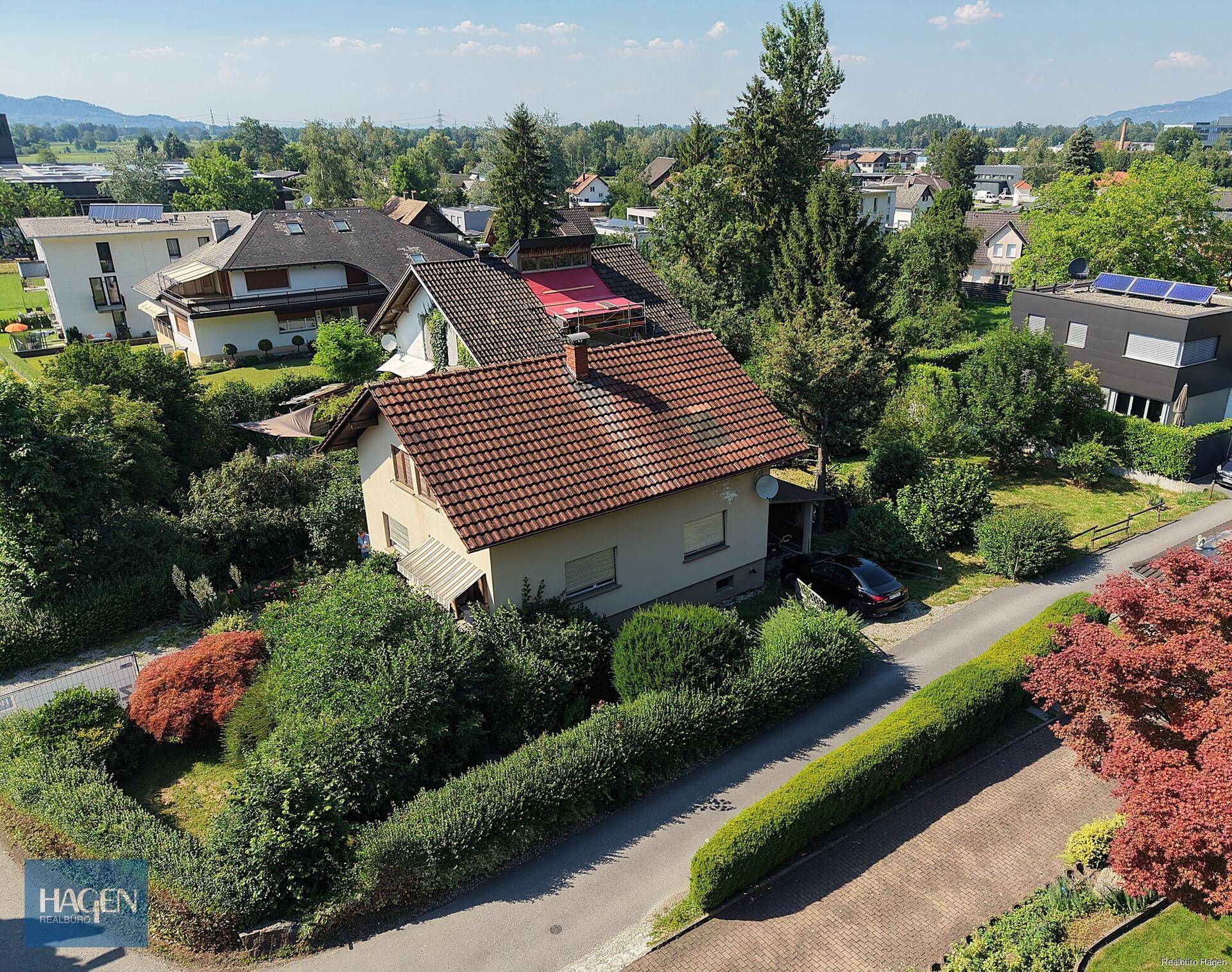Panoramablick auf ein Wohnhaus mit Garten, Balkon und die umliegende grüne Landschaft.