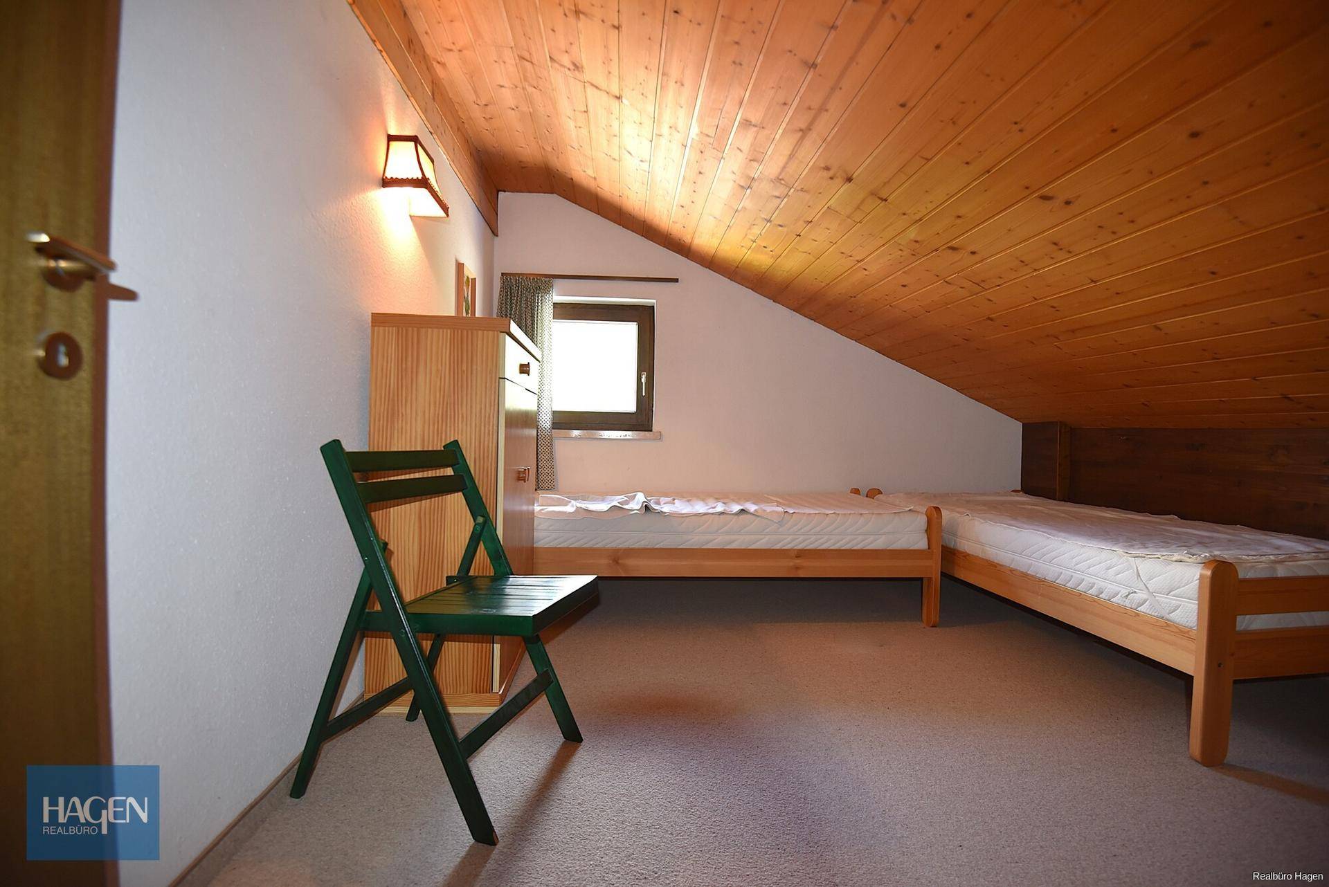 Dachschlafzimmer mit Holzbalkendecke, zwei Einzelbetten und einem kleinen Fenster für natürliches Licht.