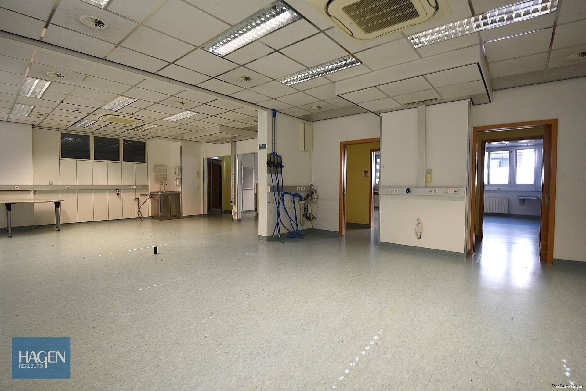Großer Arbeitsraum mit mehreren Türen, sichtbaren Installationen und heller Beleuchtung.