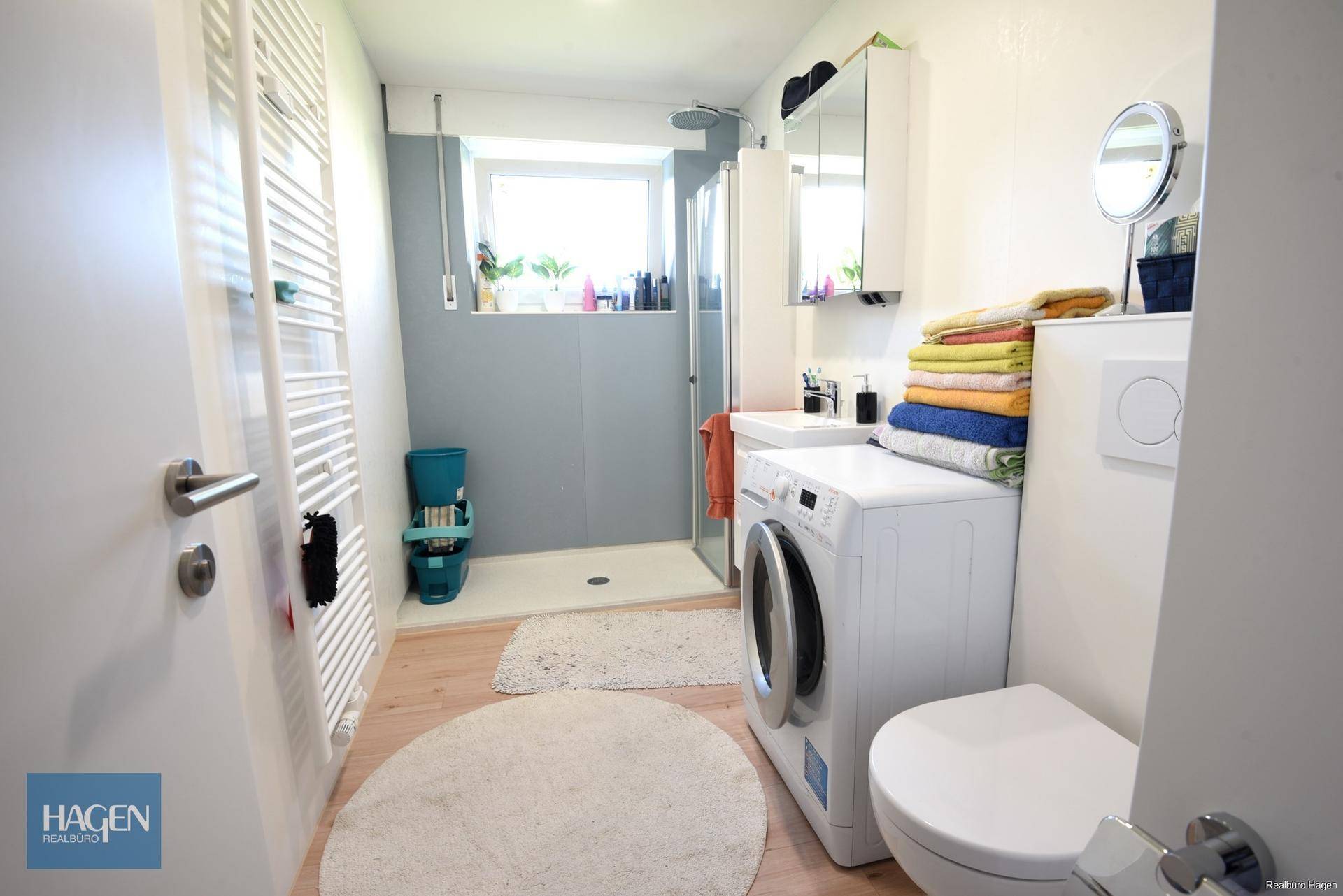 Modernes Badezimmer mit Dusche, WC, Waschbecken und Waschmaschine, inklusive Fenster.