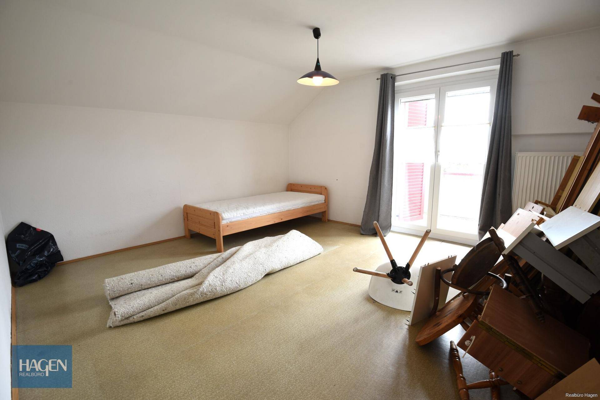 Dachgeschosszimmer mit schrägen Wänden, Einzelbett und Fenster mit roten Fensterläden.