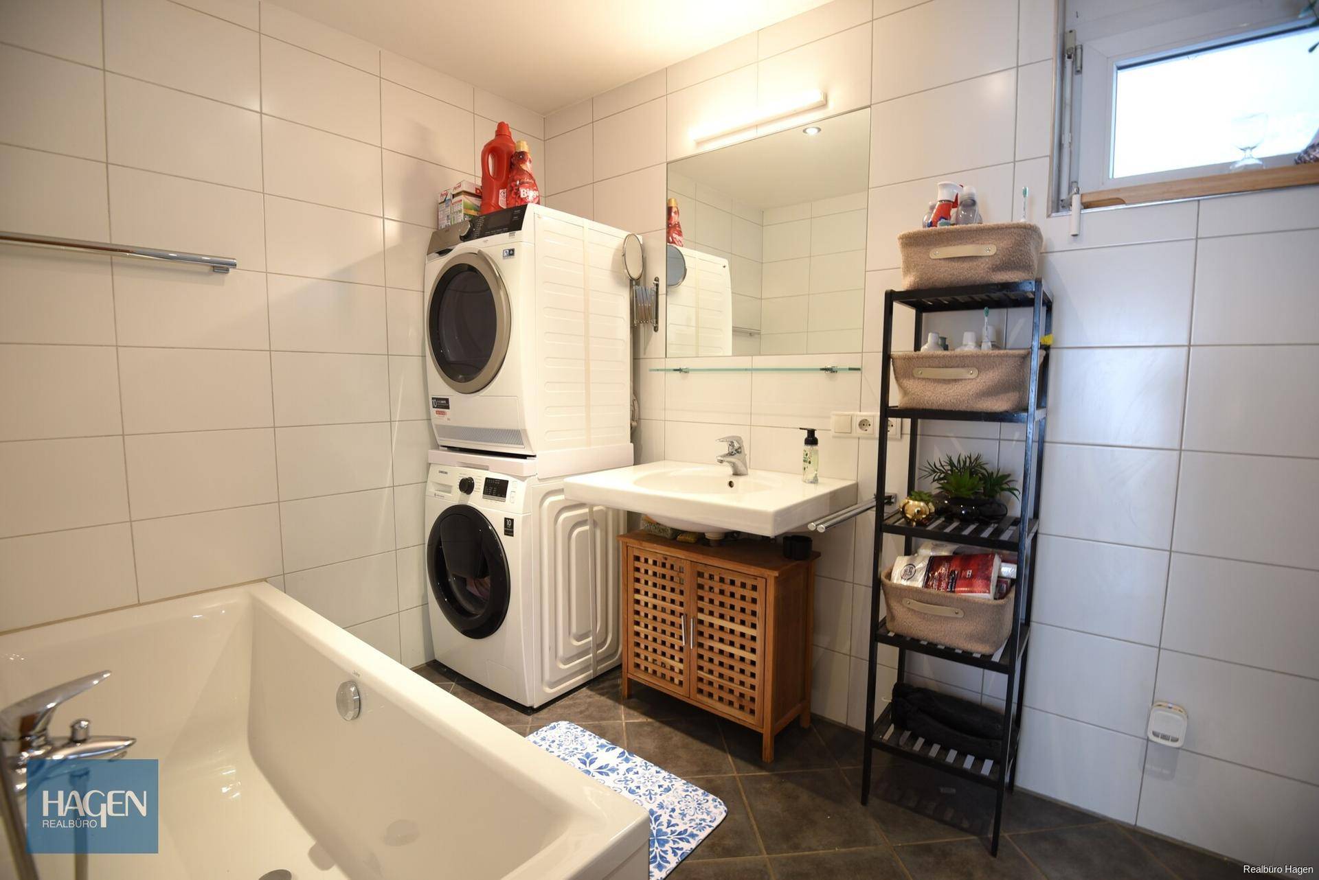 Badezimmer mit Badewanne, Waschmaschine und Trockner sowie einem Fenster.