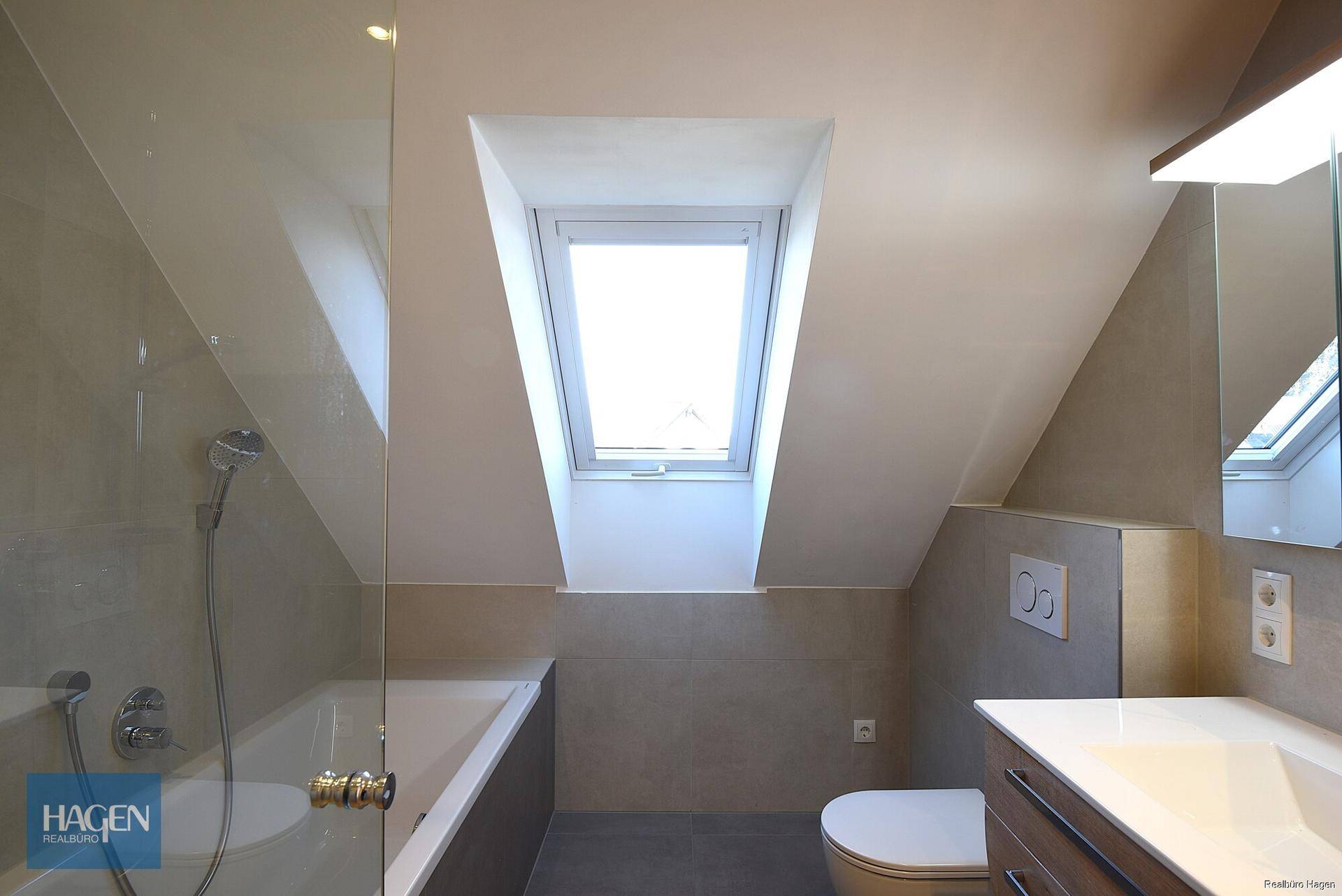 Helles Badezimmer mit Badewanne, WC, Einzelwaschbecken und Dachfenster in der Dachschräge.