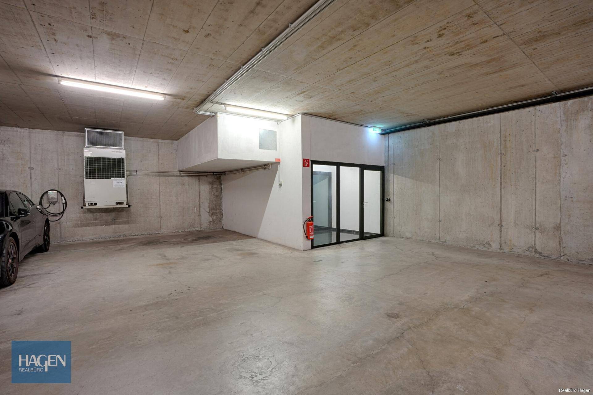 Geräumige Tiefgarage mit Betonboden, einem geparkten Auto und Zugang zum Gebäude.