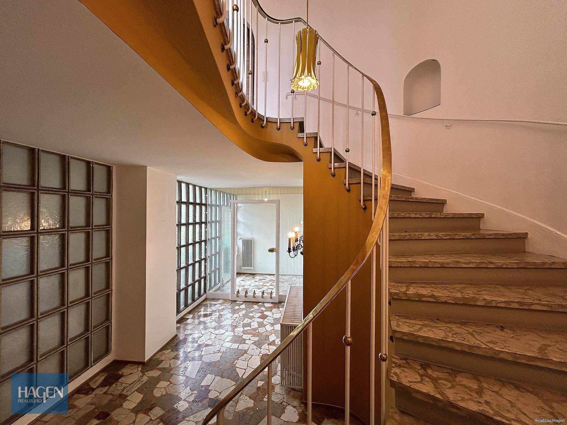 Eindrucksvolles Treppenhaus mit geschwungener Wendeltreppe, Marmorstufen und Glasbausteinwand.