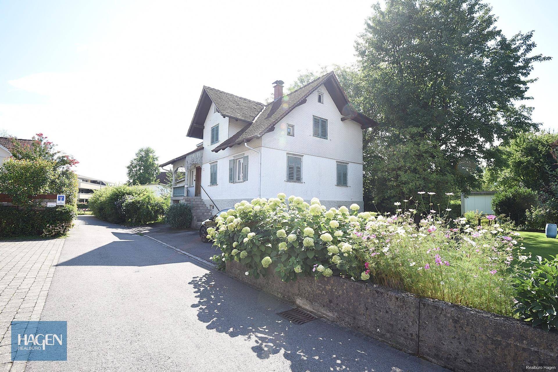 Vorderansicht des Hauses mit weißer Fassade, grünen Fensterläden und blühenden Hortensien im Vorgarten.