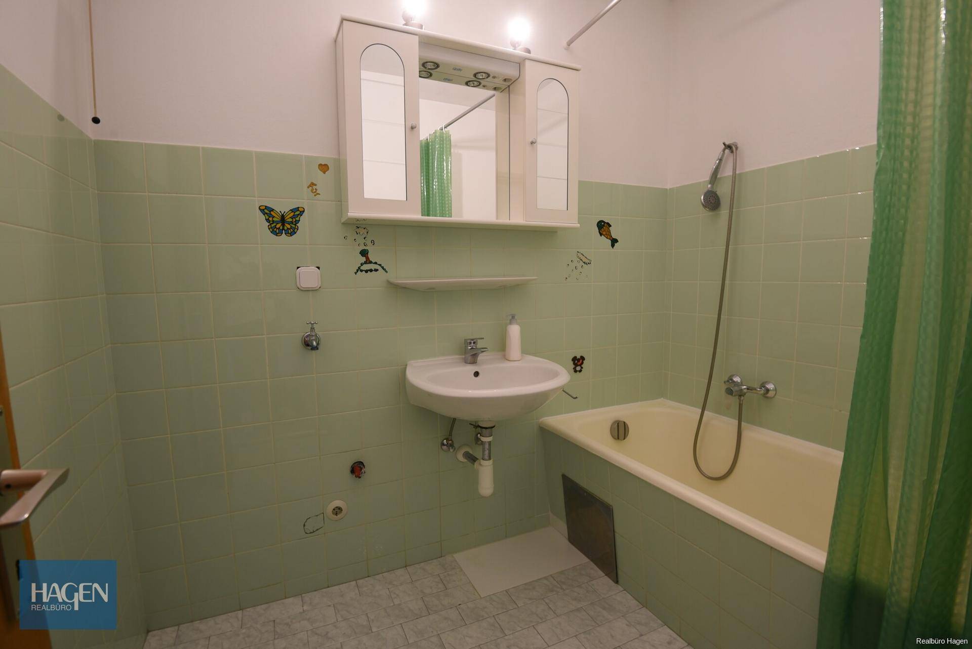 Badezimmer mit mintgrünen Fliesen, Badewanne und Waschbecken.