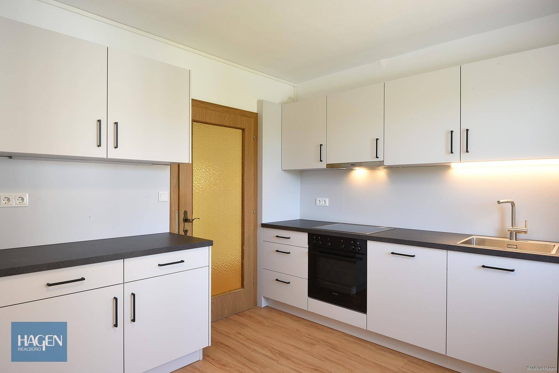 Helle Küche mit weißen Schränken, dunkler Arbeitsplatte, integrierten Geräten und Laminatboden.