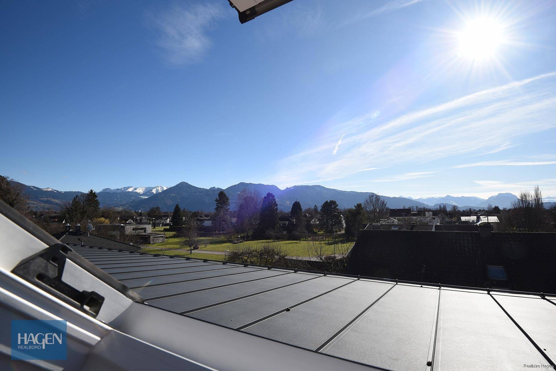 Weitblick über die Dächer mit Solaranlage, grünen Flächen und beeindruckendem Bergpanorama.