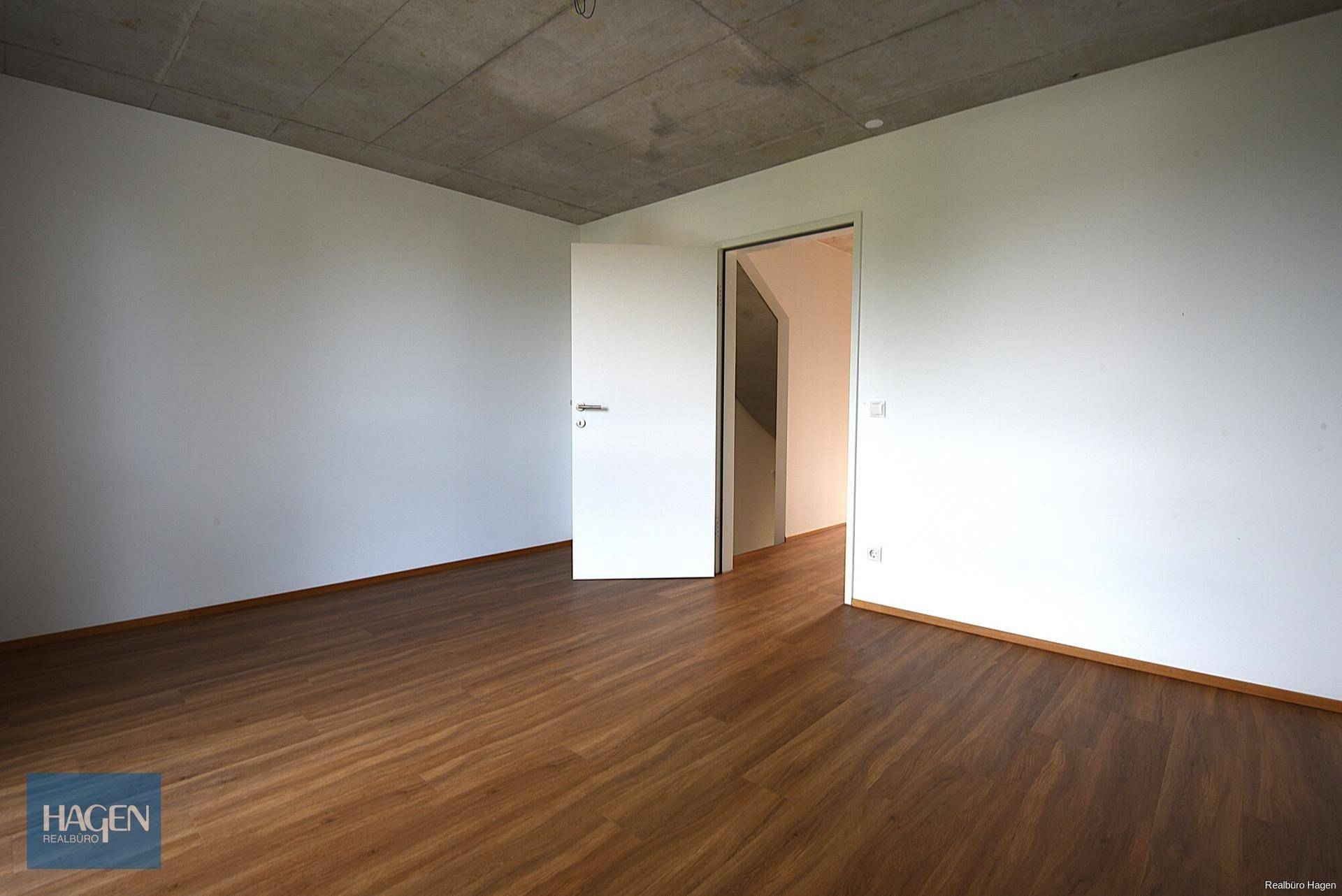 Leerer Raum mit Laminatboden und weißen Wänden, bereit zur individuellen Gestaltung.