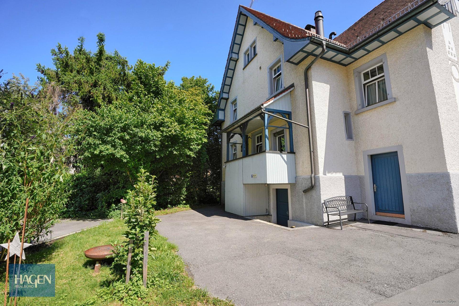 Seitenansicht des Hauses mit breiter Zufahrt, Gartenbereich und üppigem Grün.