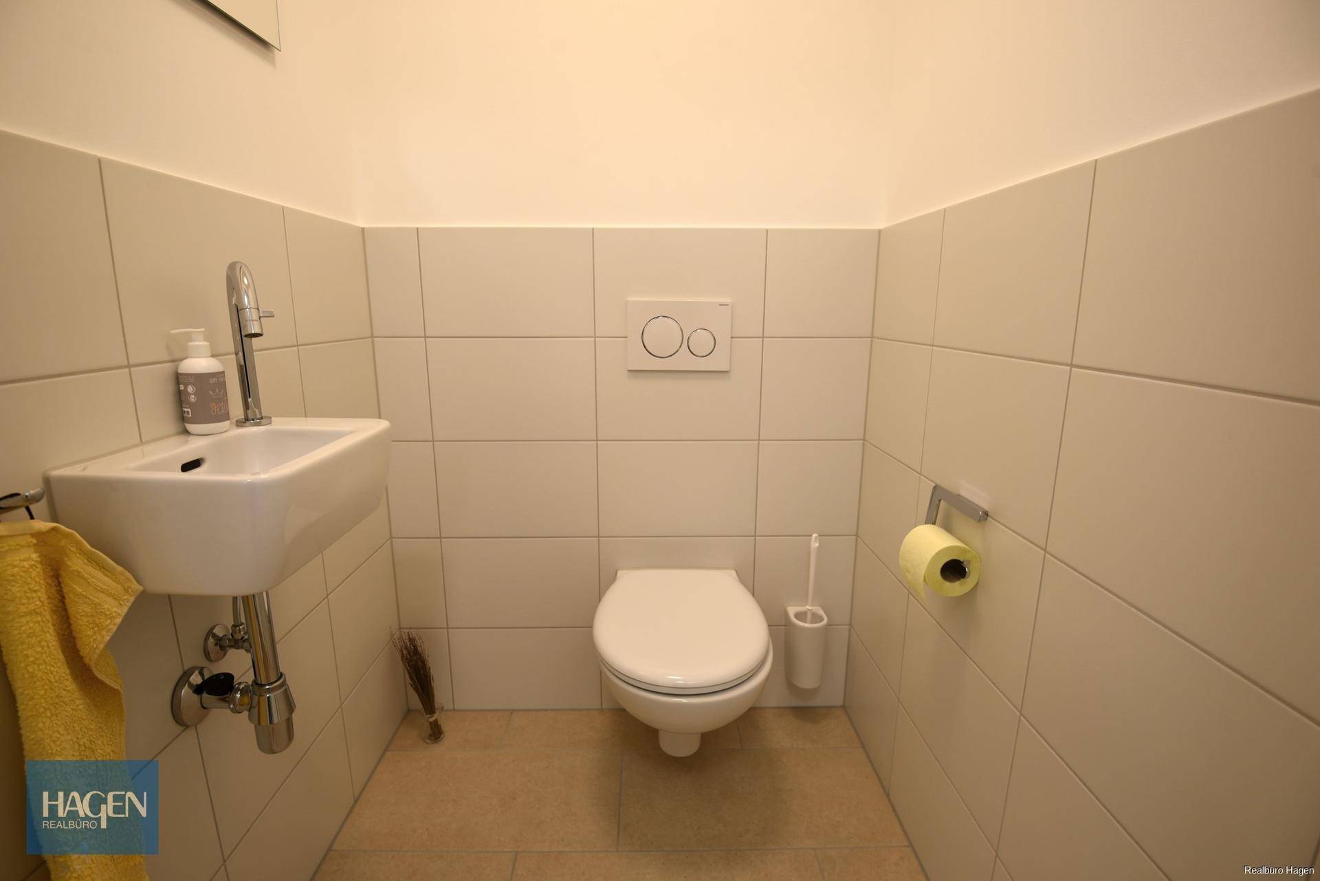 Modernes Gäste-WC mit weißen Fliesen, wandhängender Toilette und kleinem Handwaschbecken.