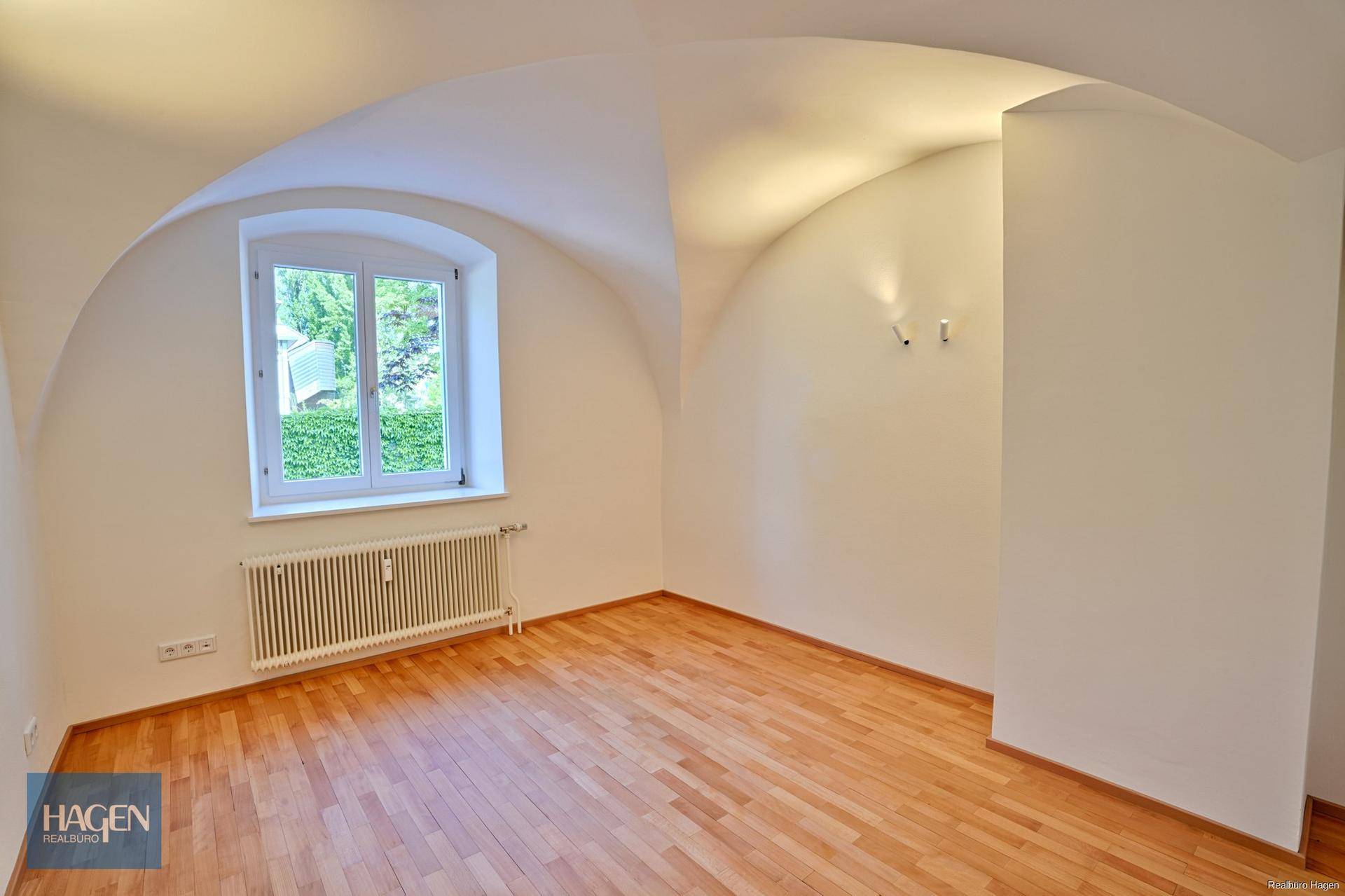 Leeres Zimmer mit Gewölbedecke, Dielenboden, weißen Wänden und einem Fenster.
