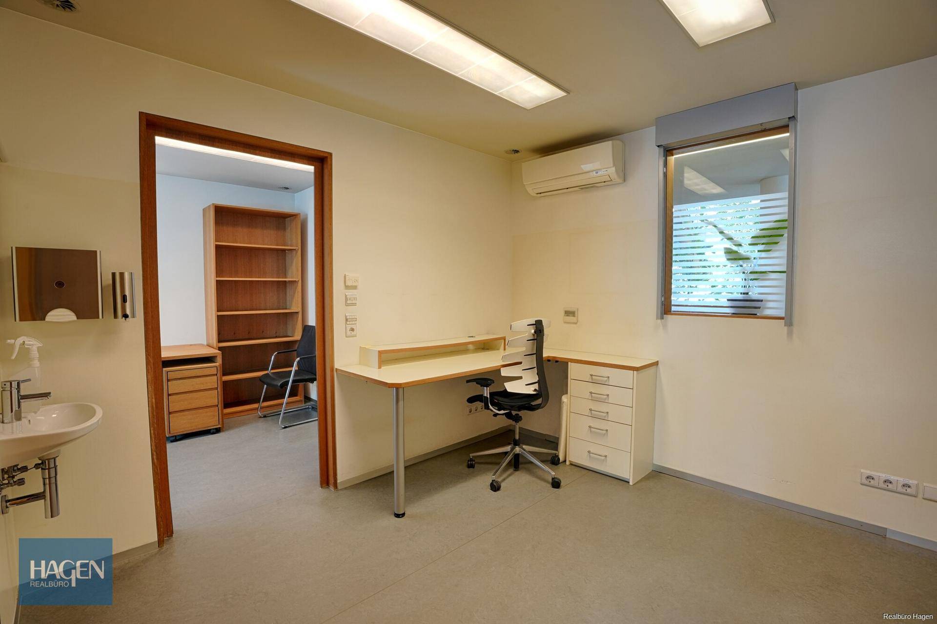 Einzelbüro mit Schreibtisch, Waschbecken und Klimaanlage, bereit zur Nutzung.