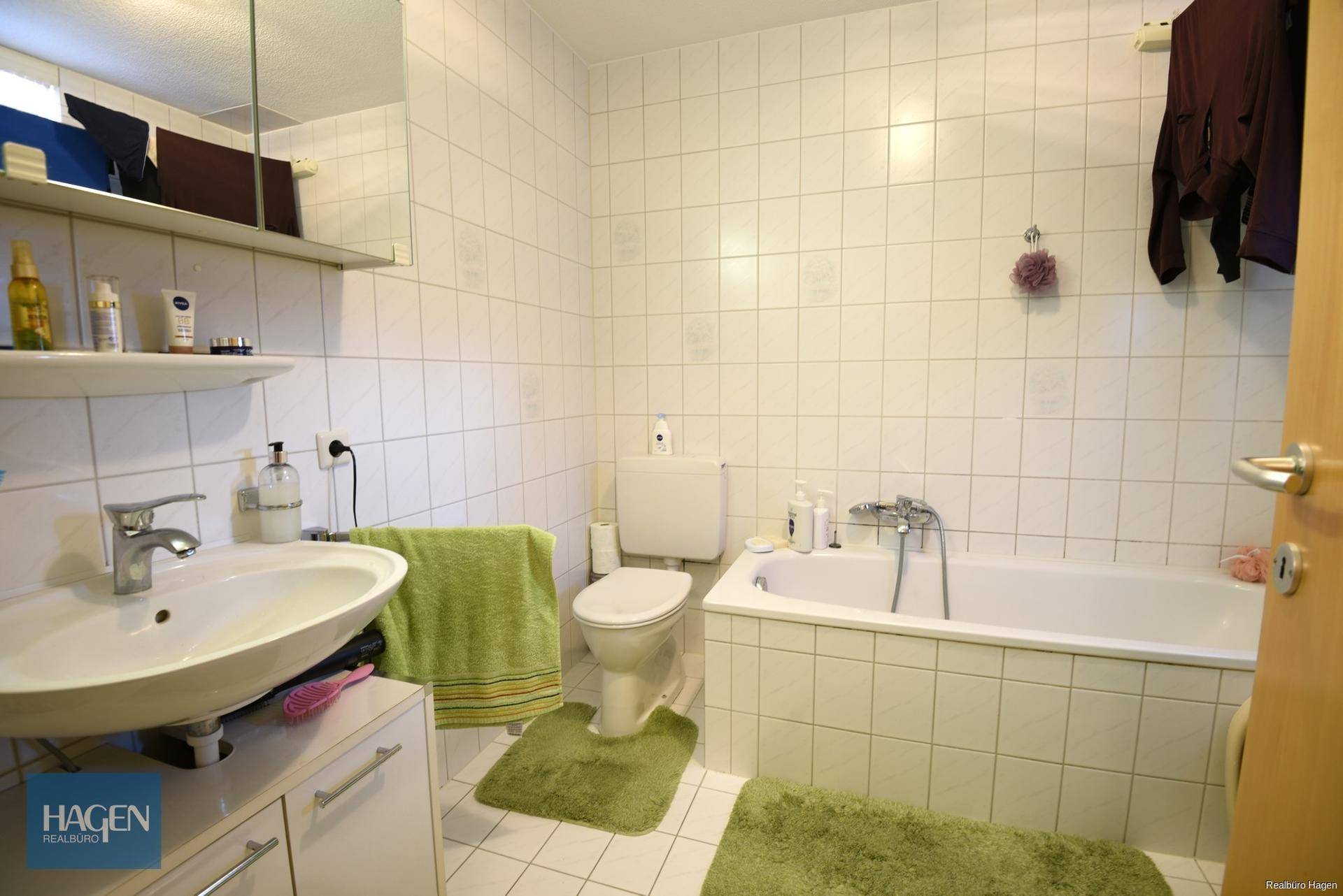 Gefliestes Badezimmer mit Badewanne, WC, Waschbecken und grünen Akzenten.