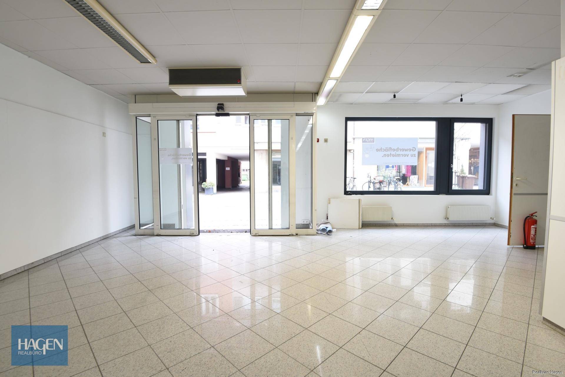 Blick vom Innenraum auf den Eingangsbereich mit automatischen Schiebetüren und großen Schaufenstern.