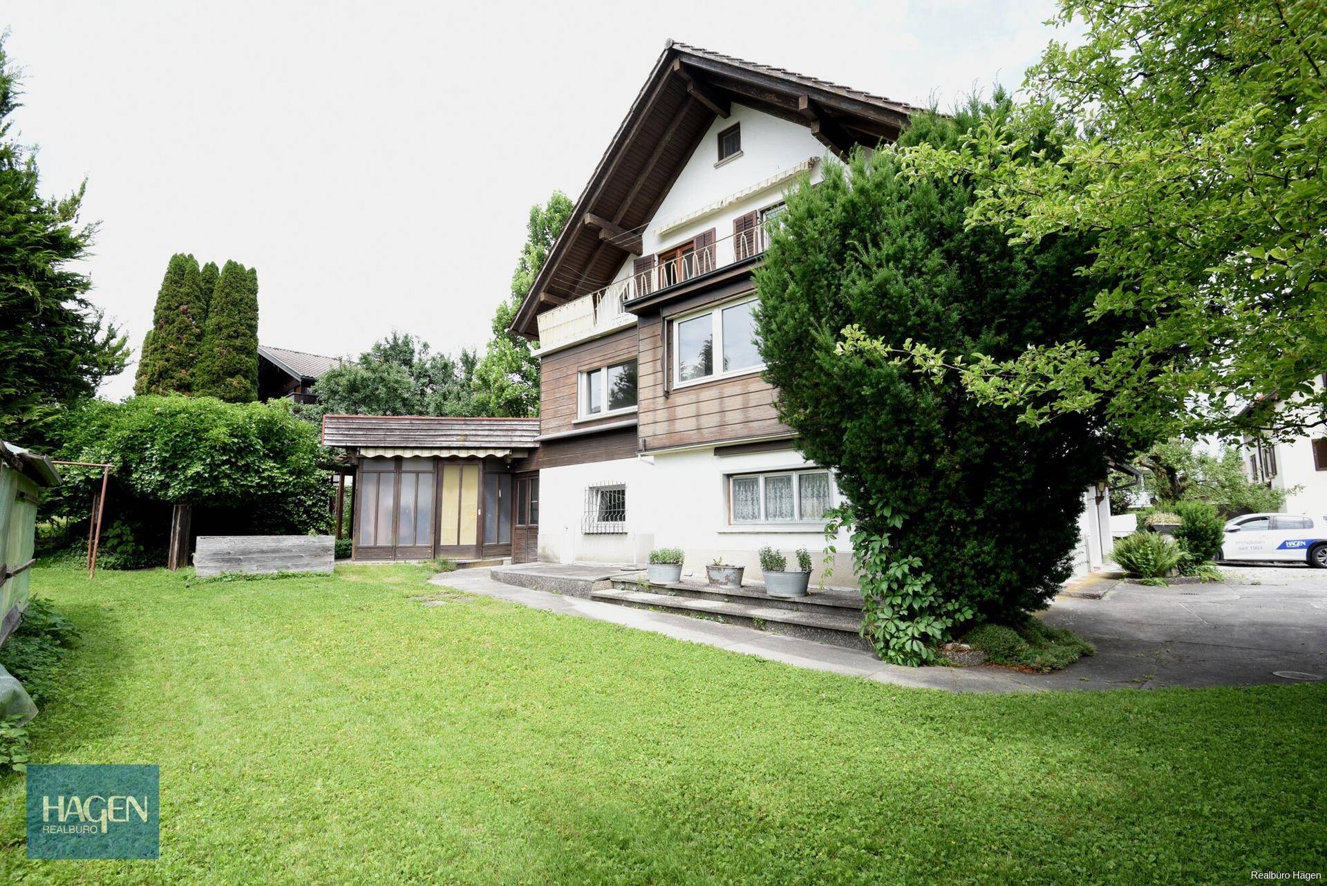 Seitenansicht des Hauses mit gepflegtem Rasen, Bäumen und einem kleinen Anbau.