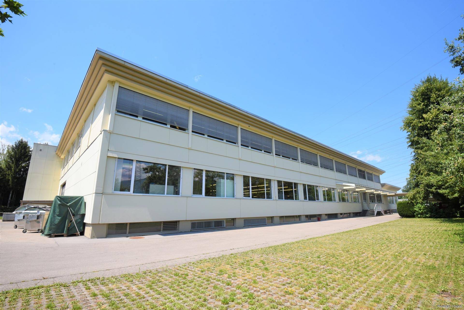 Moderne Gebäudefassade mit vielen Fenstern, umgeben von Grünflächen unter blauem Himmel.