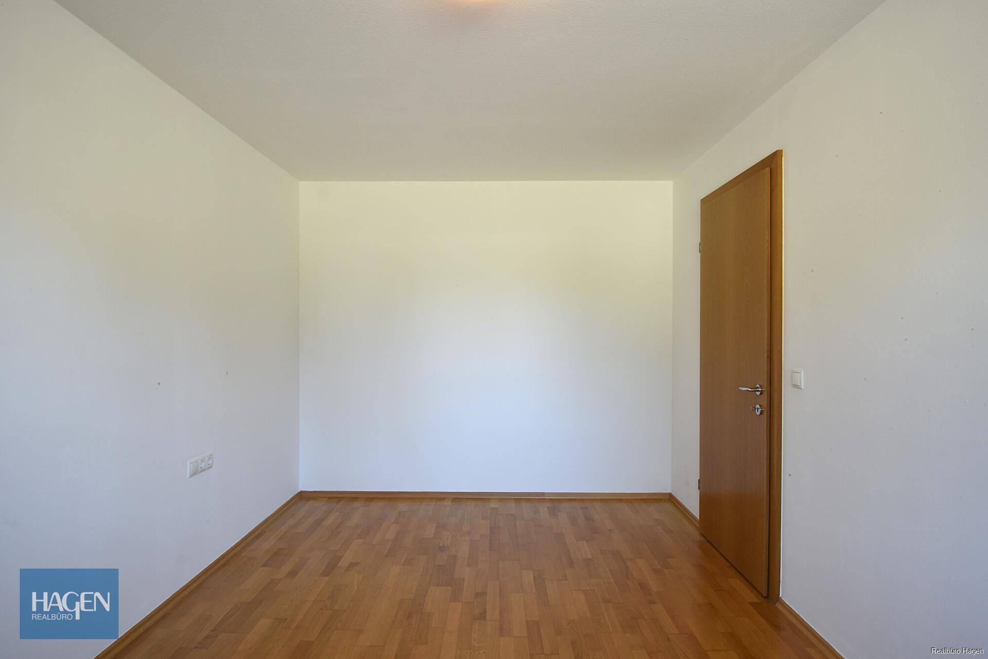 Leeres Zimmer mit Parkettboden und einfacher Holztür, bereit zur individuellen Gestaltung.