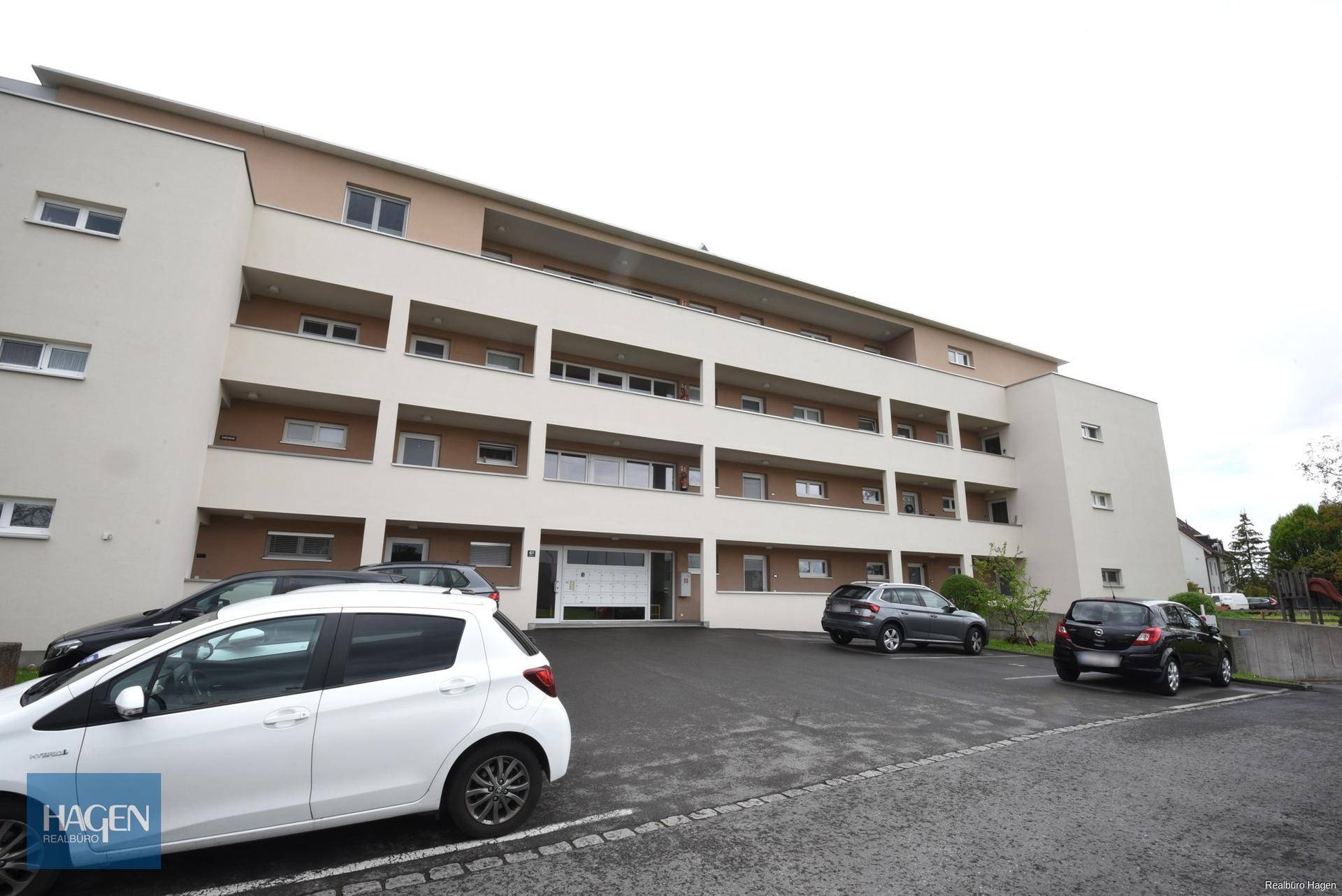 Modernes Mehrfamilienhaus mit mehreren Etagen und Außenparkplätzen vor dem Gebäude.