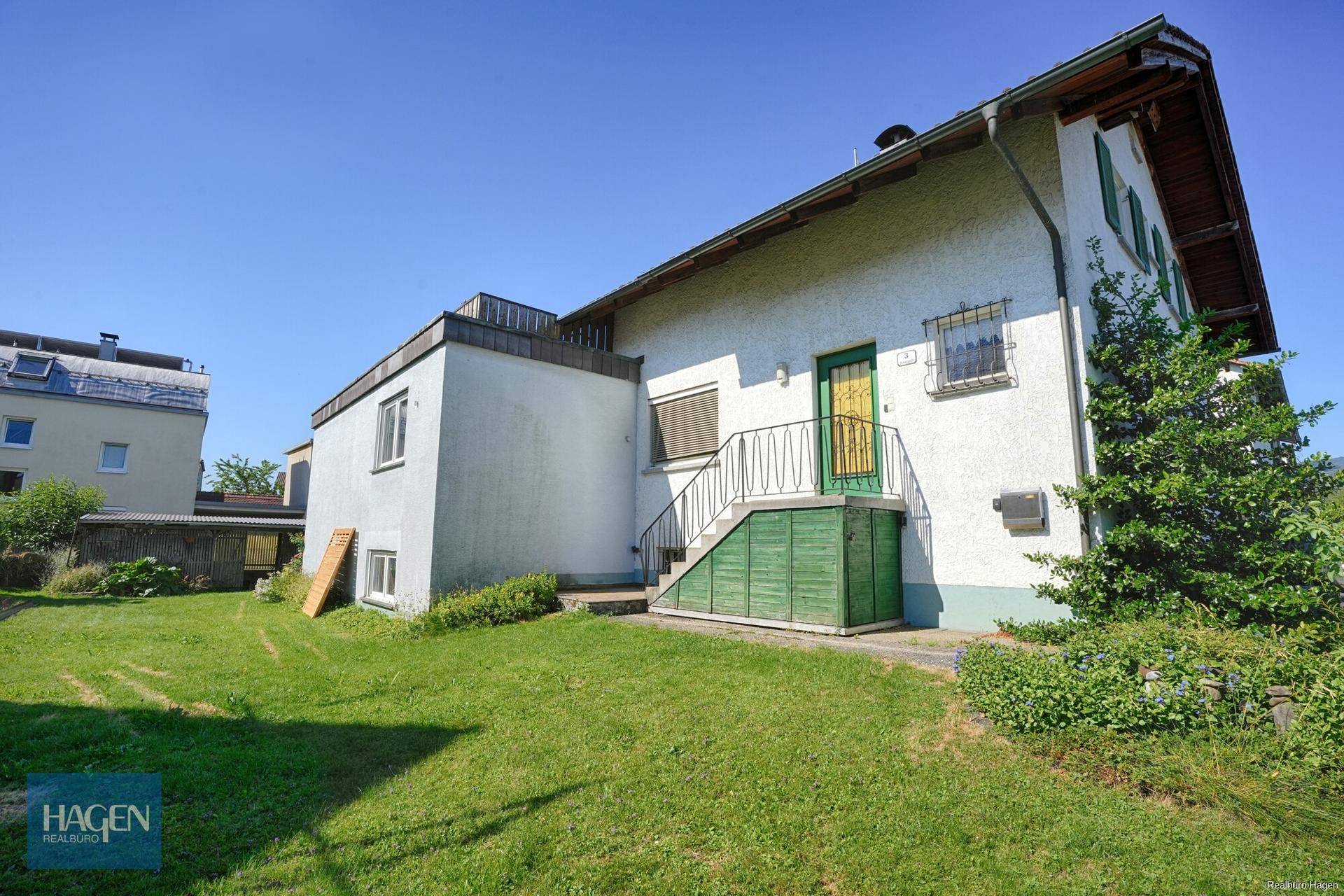 Seitenansicht des Hauses mit Rasenfläche, Außentreppe und Nebengebäude.