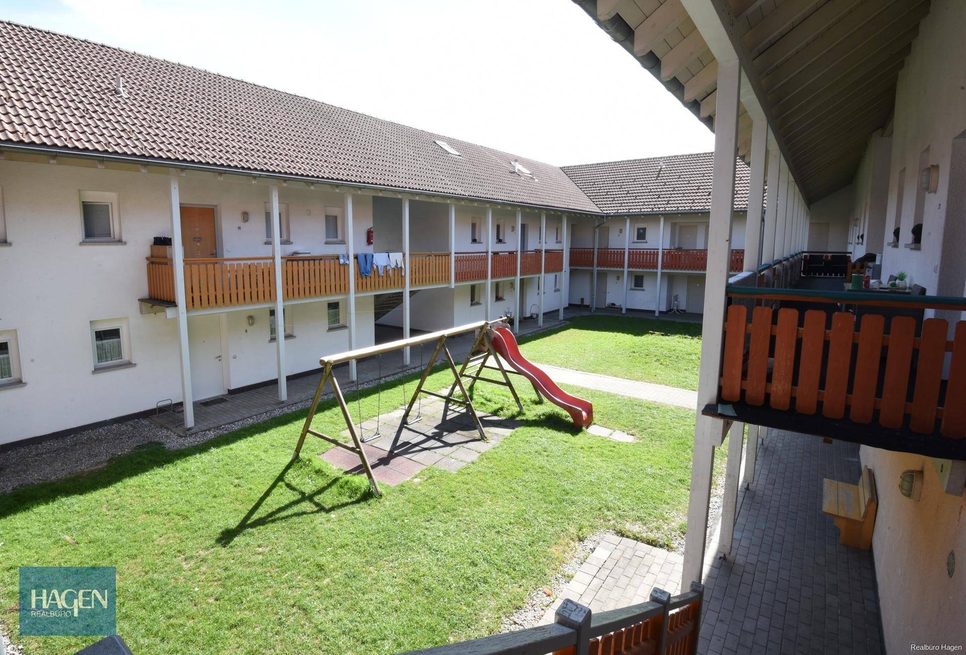 Innenhof mit Grünfläche, Kinderspielplatz und umlaufenden Balkonen.