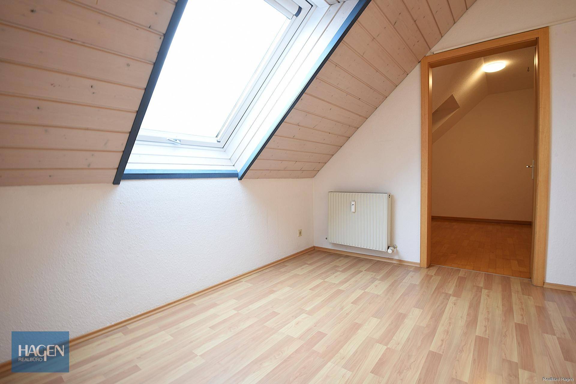 Dachbodenraum mit Dachfenster, Heizkörper und Zugang zu einem weiteren Zimmer.