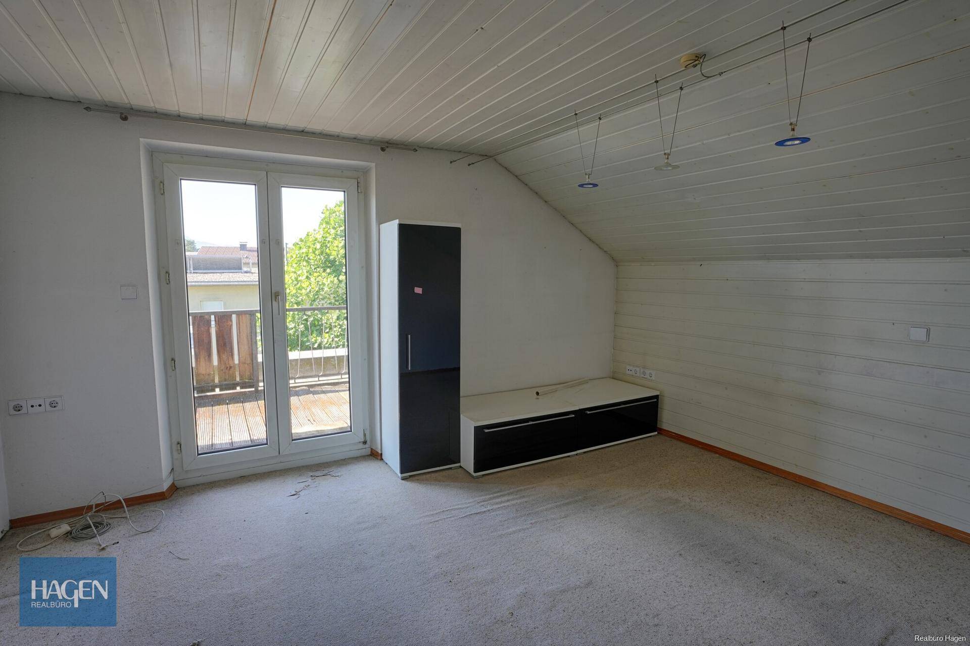 Helles Dachgeschosszimmer mit Schrägen, Teppichboden und Balkonzugang.