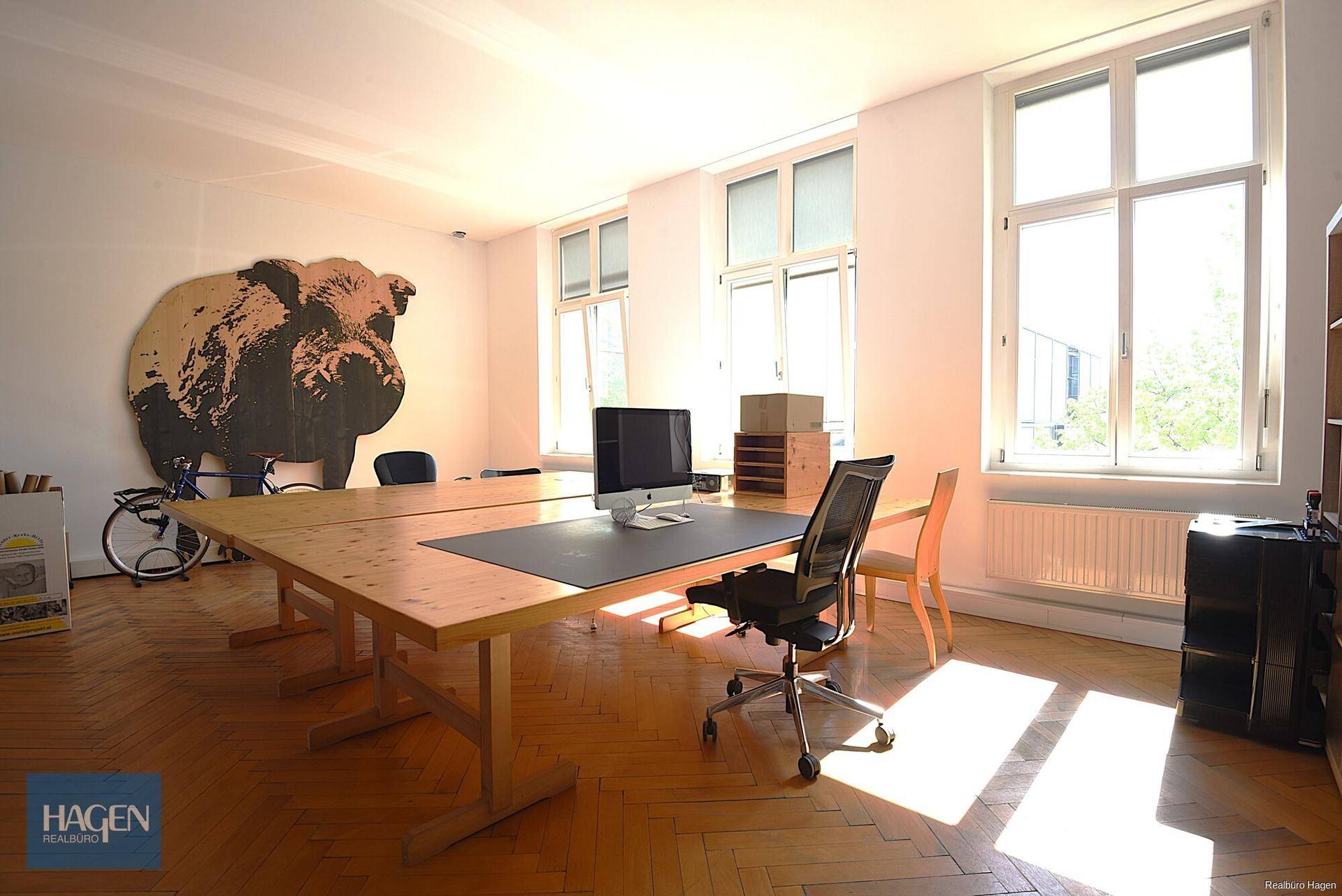 Helles Büro mit großem Holztisch, ergonomischen Stühlen und einem dekorativen Wandbild, beleuchtet von Sonnenlicht.