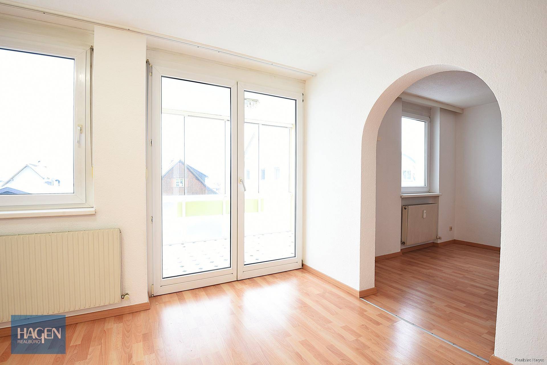 Heller Raum mit Laminatboden, Zugang zum Wintergarten und einem Rundbogen.