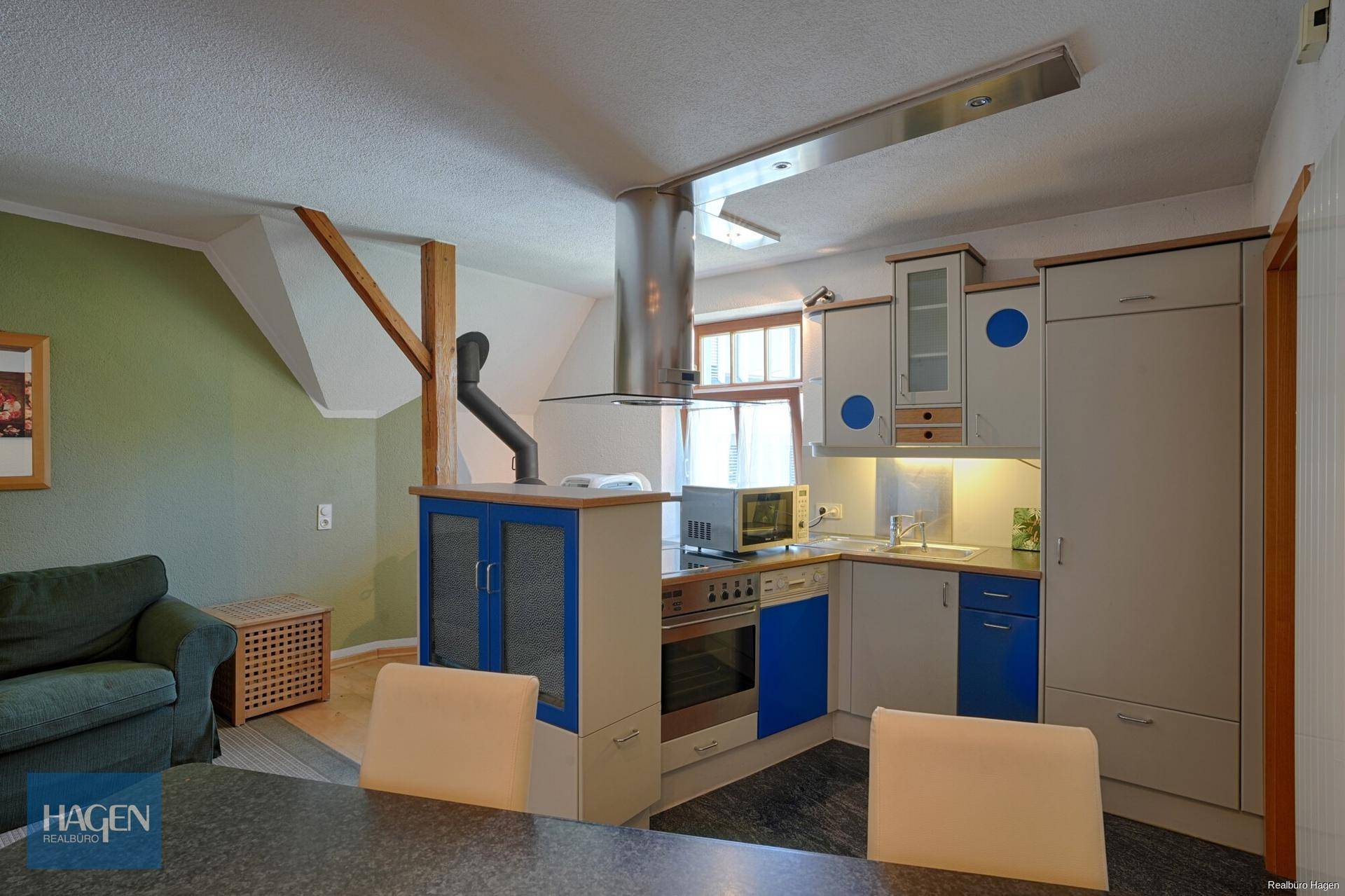 Kompakte Küche im Dachgeschoss mit blauen Akzenten, Dunstabzugshaube und Essbereich.