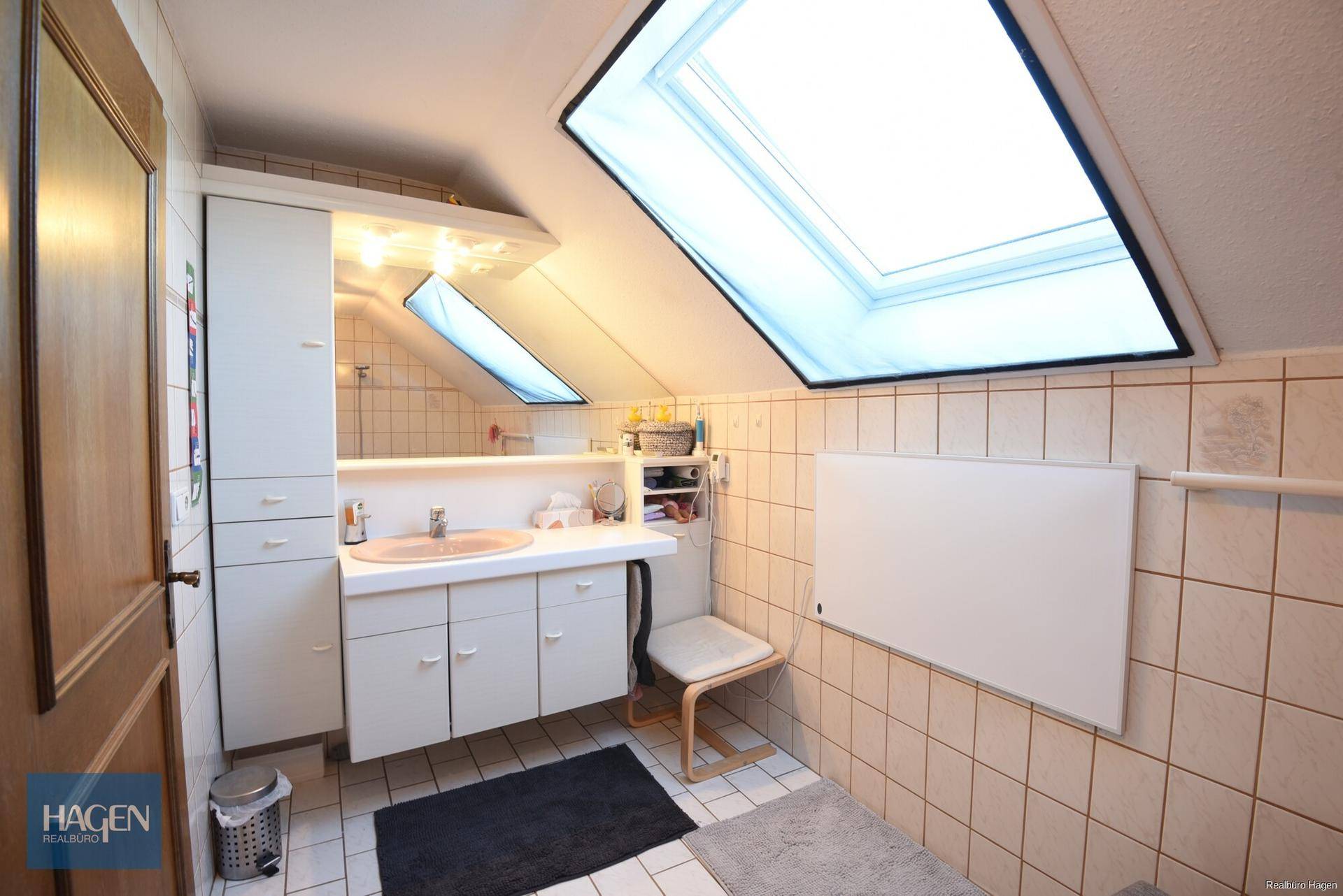 Badezimmer im Dachgeschoss mit Dachfenstern, Waschtisch und hellen Fliesen.