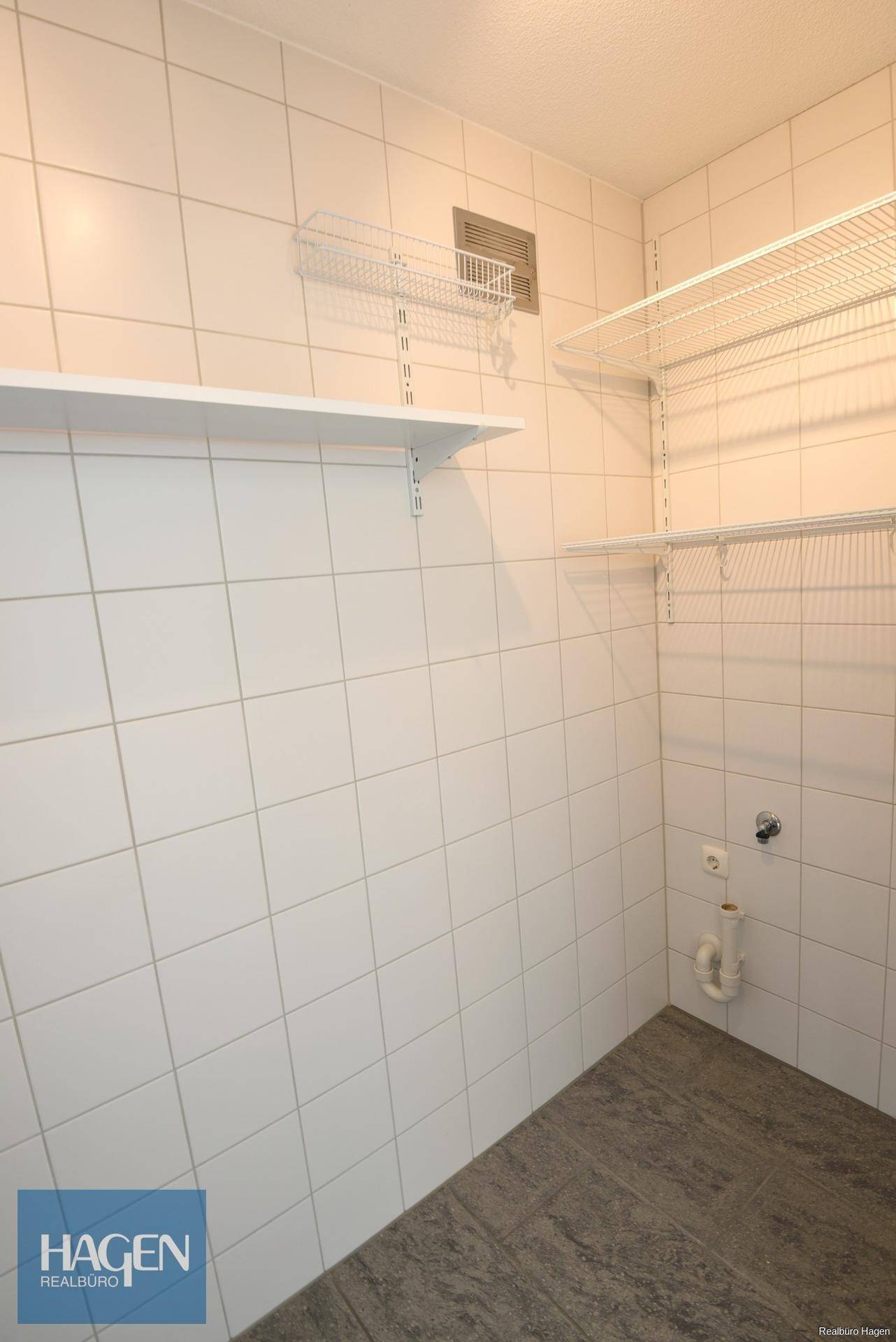 Praktischer Abstellraum mit Fliesenwänden, Regalen und Anschlüssen für Waschmaschine.