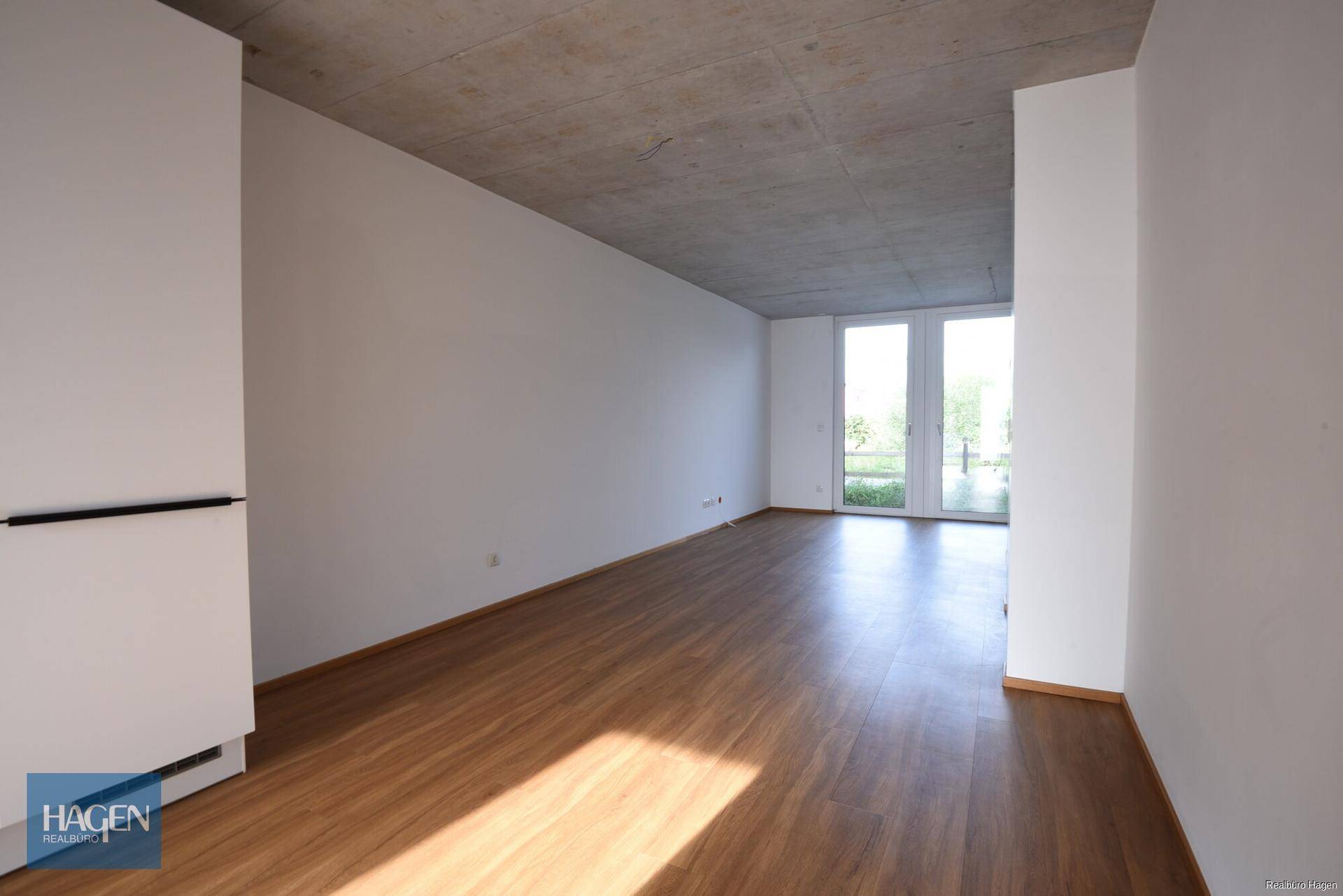 Heller Wohnbereich mit Laminatboden, hohen Decken und integriertem weißen Schrank.