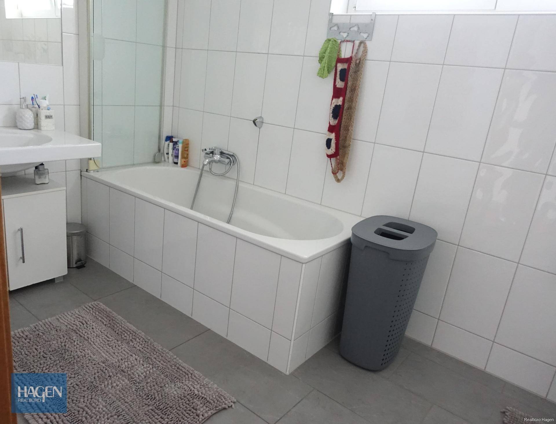 Hell gefliestes Badezimmer mit Badewanne, Duschabtrennung und modernem Waschbecken.
