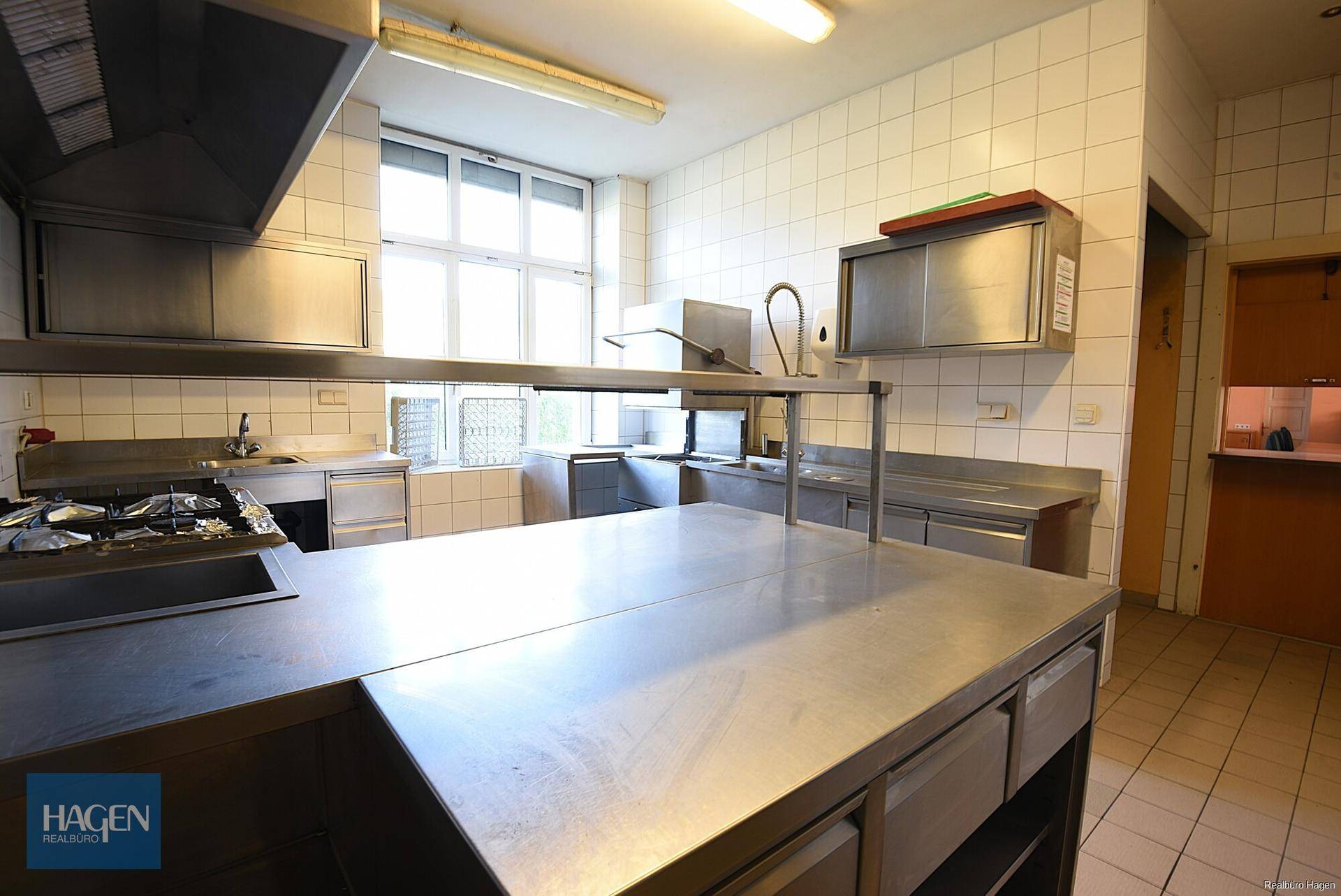 Professionelle Edelstahlküche mit großen Arbeitsflächen, Spülbecken und Ablufthaube, sehr funktional.