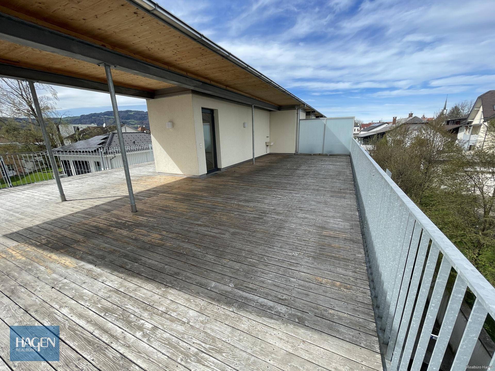 Weitläufige Holzterrasse mit Metallgeländer und Blick auf die umliegende Wohnbebauung.