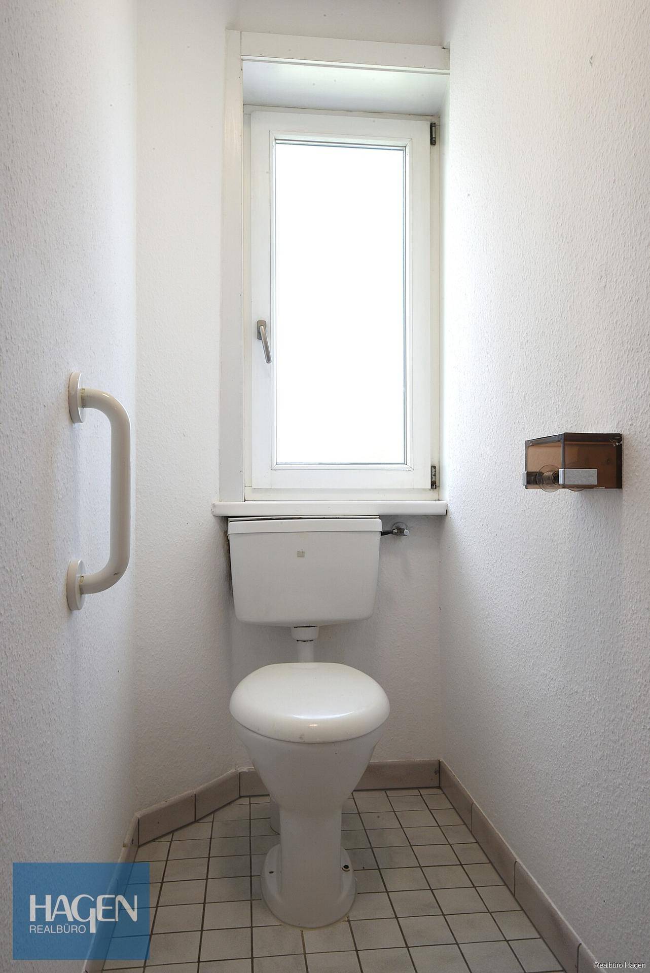 Separate Toilette mit Fenster, Fliesenboden und Haltegriff für zusätzliche Sicherheit und Komfort.