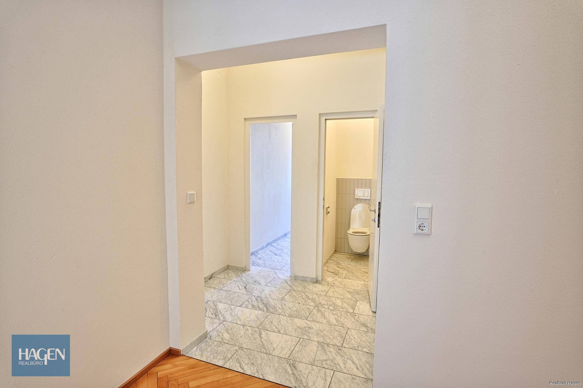 Eingangsbereich mit Fliesenboden, der zu einem kleinen Raum mit Toilette führt.