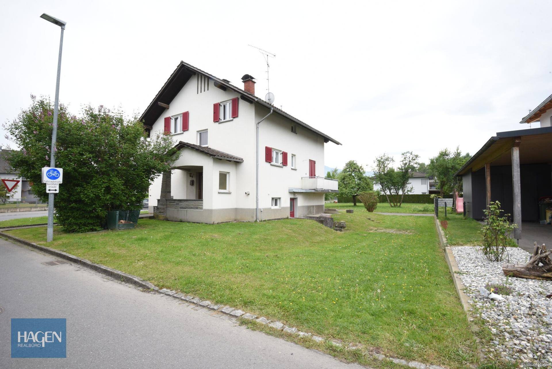 Freistehendes Haus mit Vorgarten an einer ruhigen Straße, umgeben von Grünflächen.